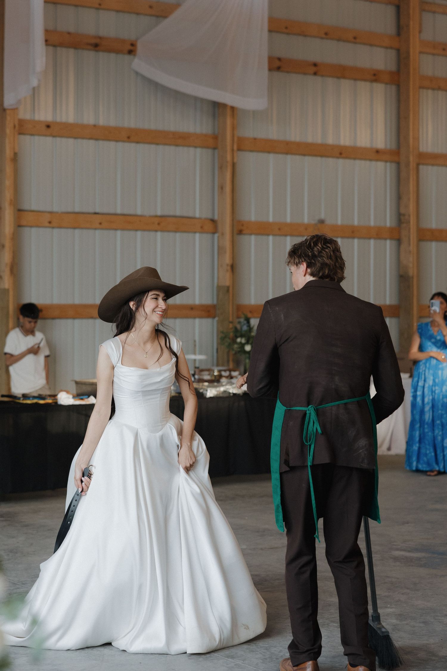 Wedding couple in formal attire dancing in an open rustic venue with wooden beams.