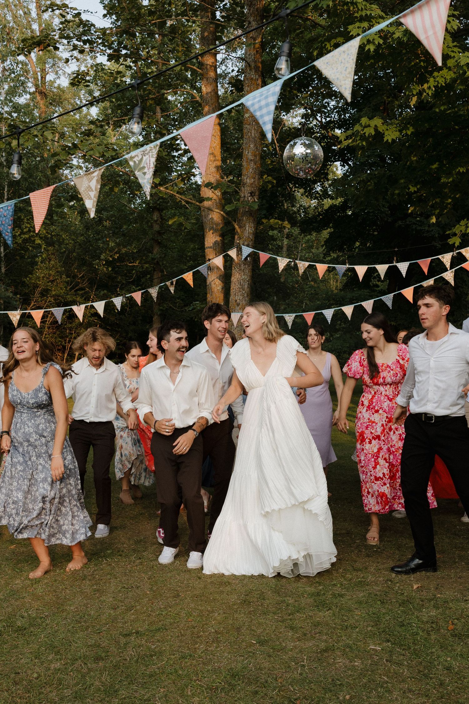 Wedding guests dancing under colorful bunting flags at an outdoor reception.
