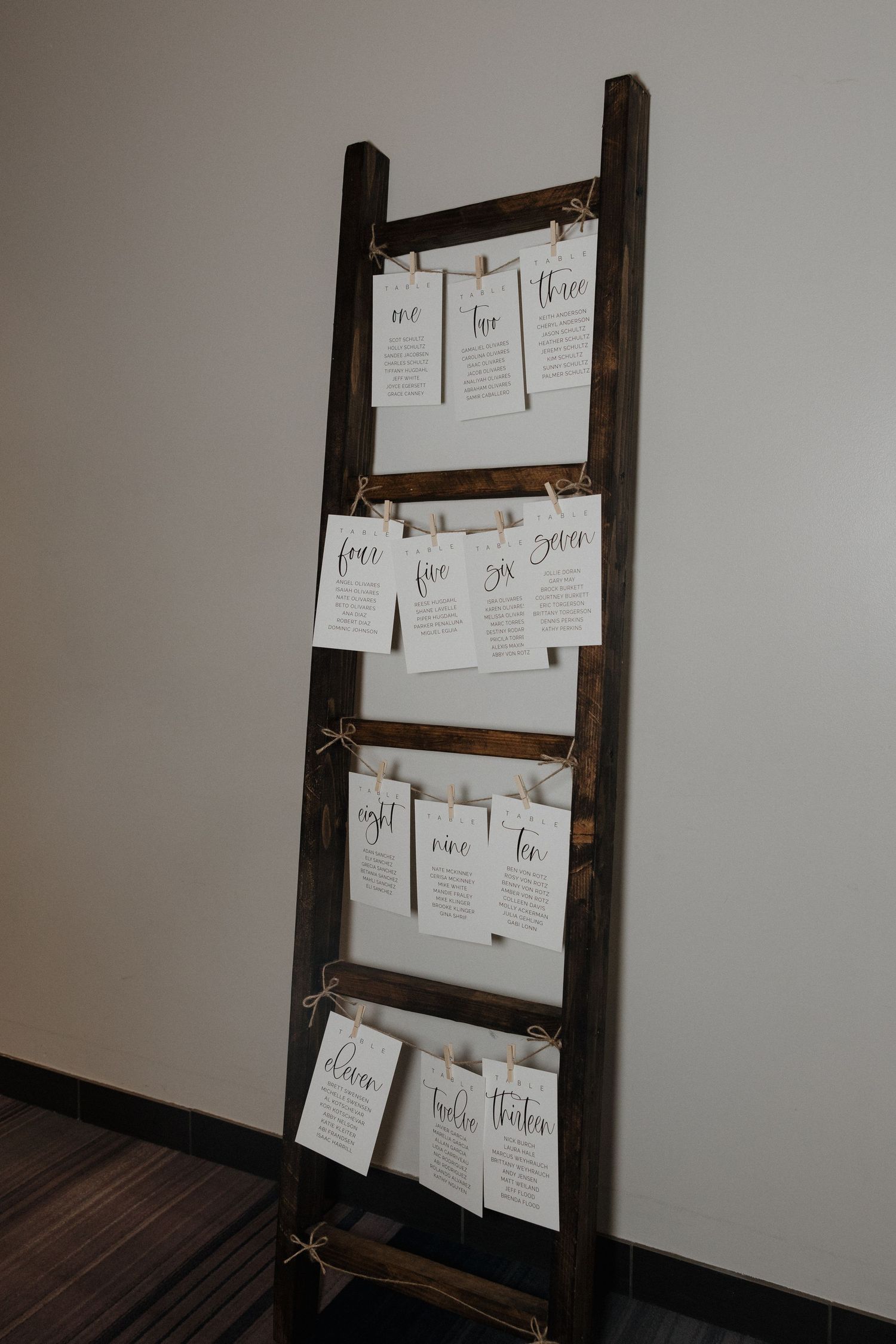 Rustic wooden ladder displaying white wedding seating cards against a neutral wall.