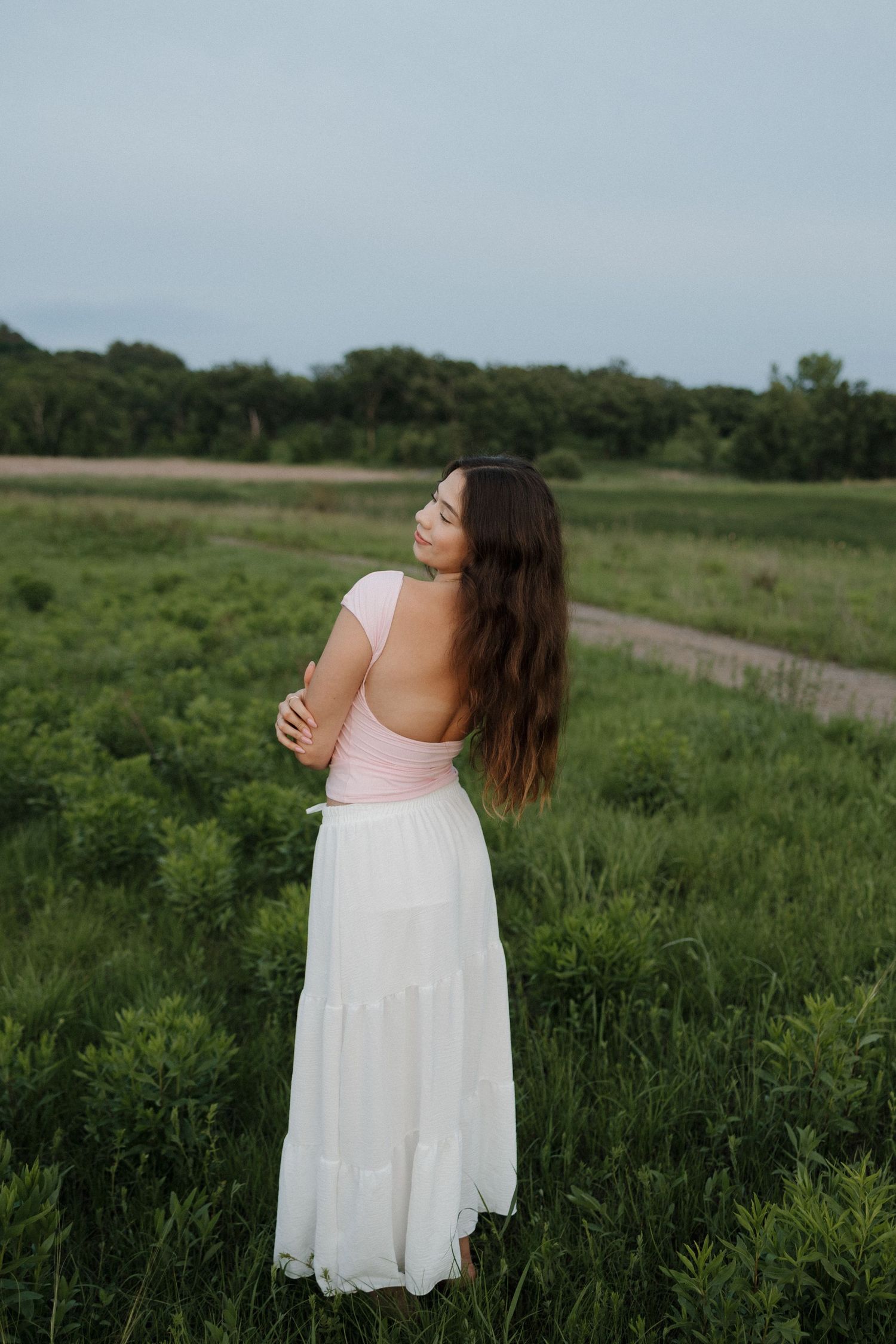 Young woman in pink top and white skirt standing in lush green field.