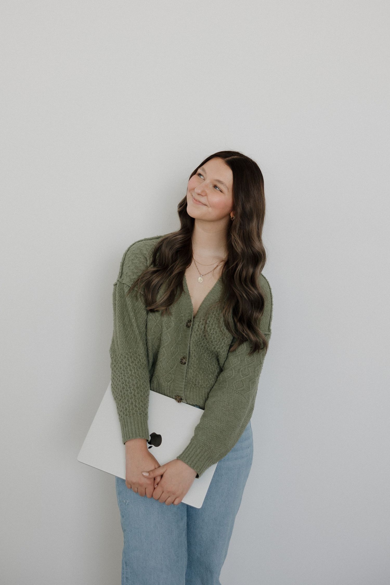 Smiling brunette woman in green cardigan holding laptop against clean white background.