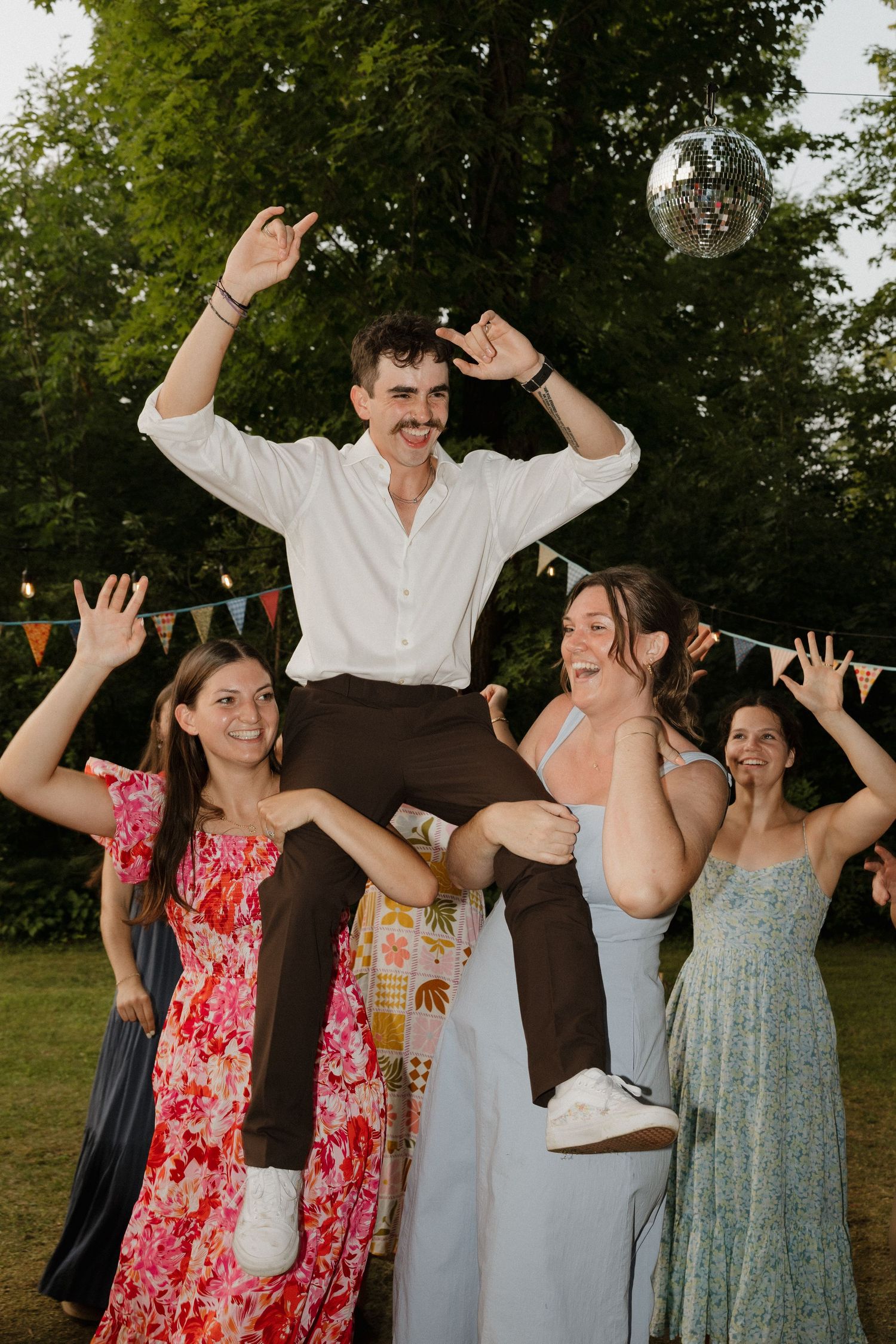 Wedding party dances joyfully at an outdoor reception under string lights.