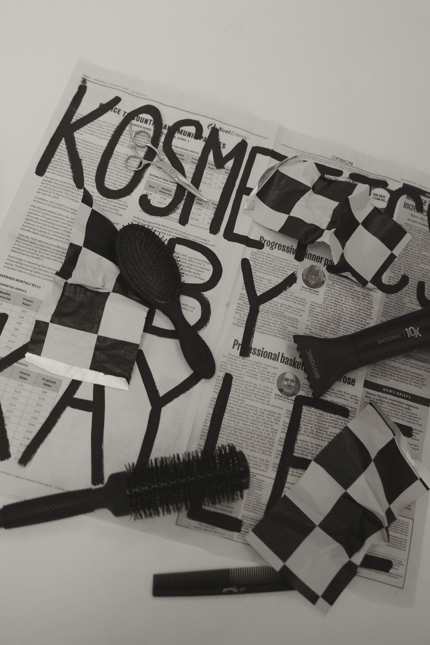 Flat lay of hair styling tools and brushes on newspaper with Kosmetics by Kaylee branding letters.