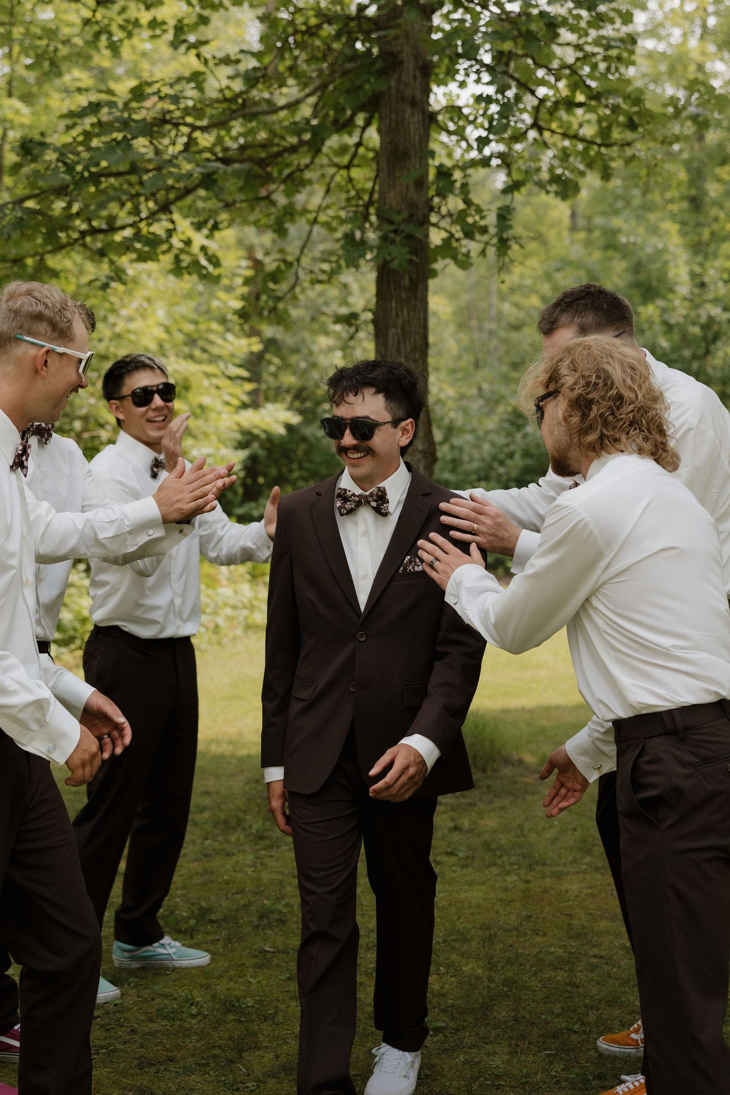 Groomsmen in black suits and bowties share a playful moment outdoors.