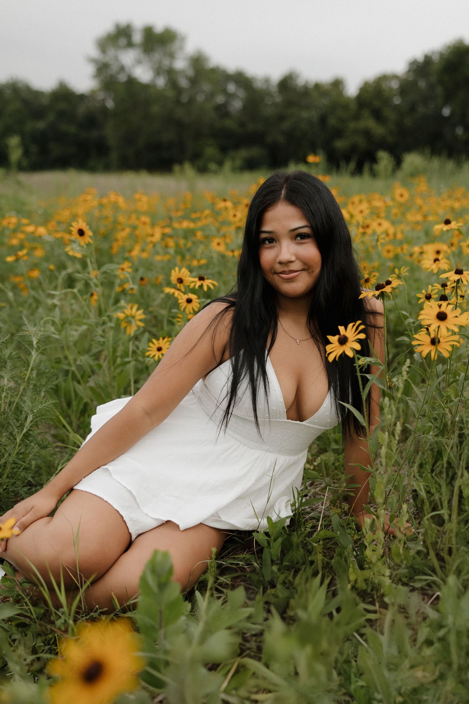 Young woman in white dress sitting among vibrant yellow black-eyed Susan wildflowers in green field.