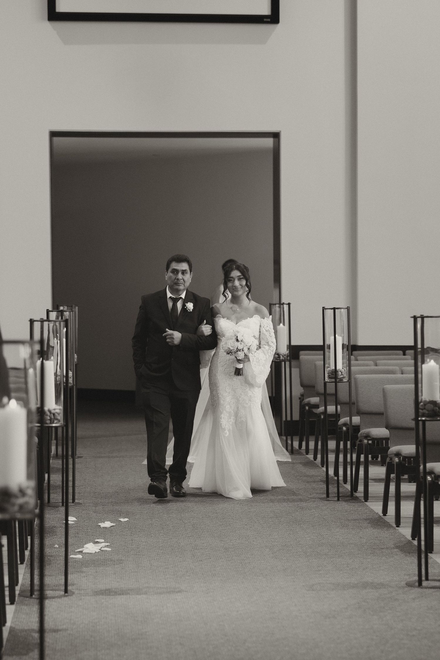 Wedding couple walking through a minimalist indoor venue with black chairs and white walls.