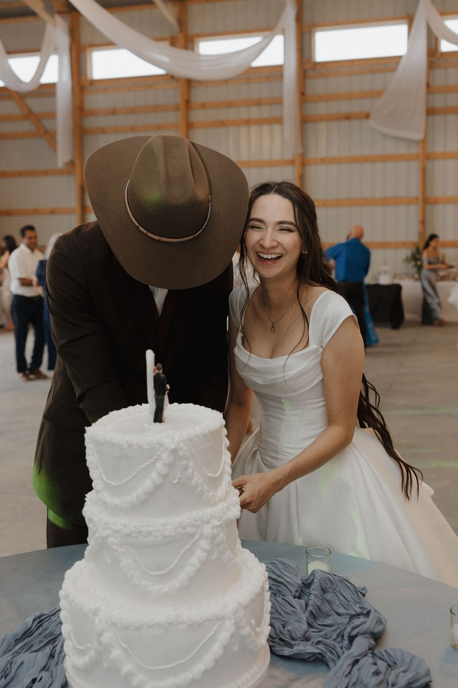 A tiered white wedding cake sits on display at an indoor venue celebration.
