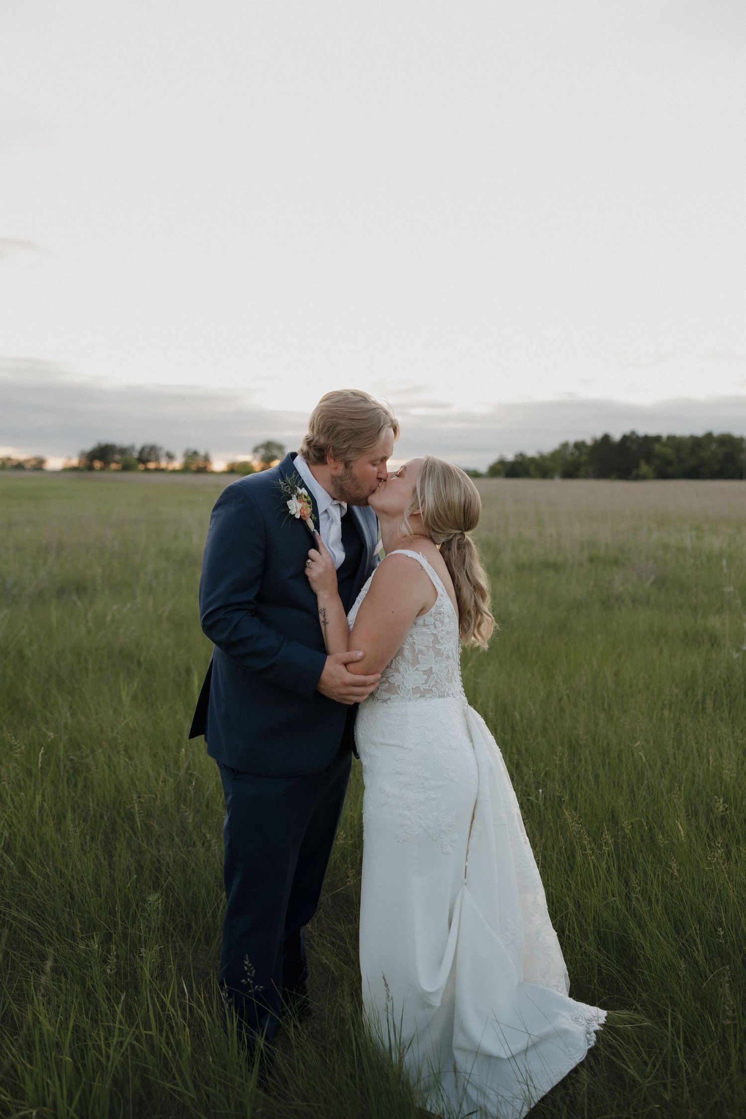 Bride and groom sharing a romantic kiss in a lush green field at sunset.