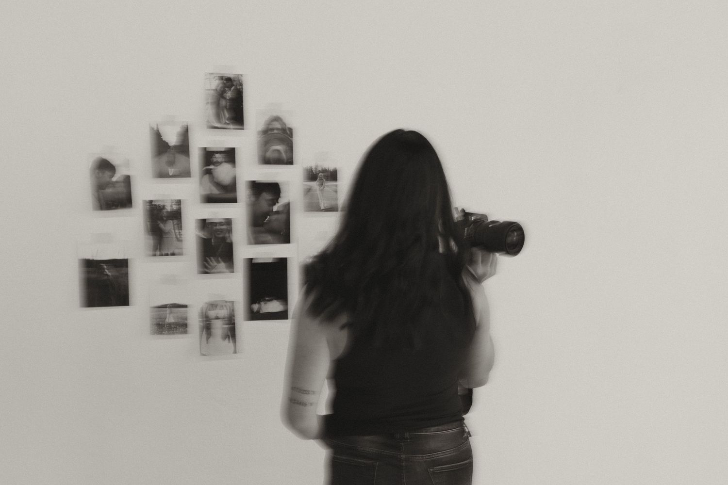 Black and white motion blur photo of woman photographing a gallery wall display of black and white prints.