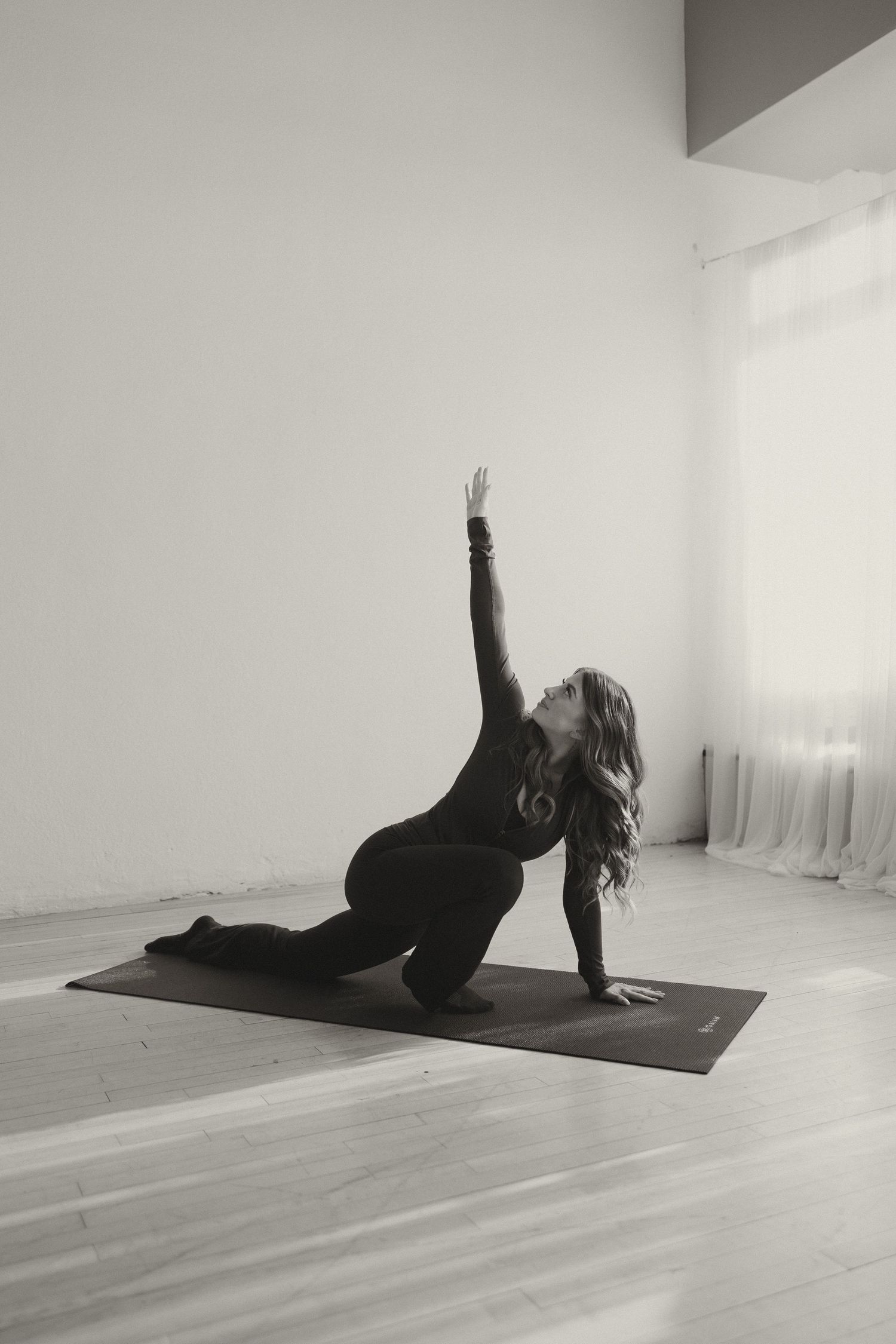 Black and white photo of woman performing a side stretch yoga pose on a mat indoors.