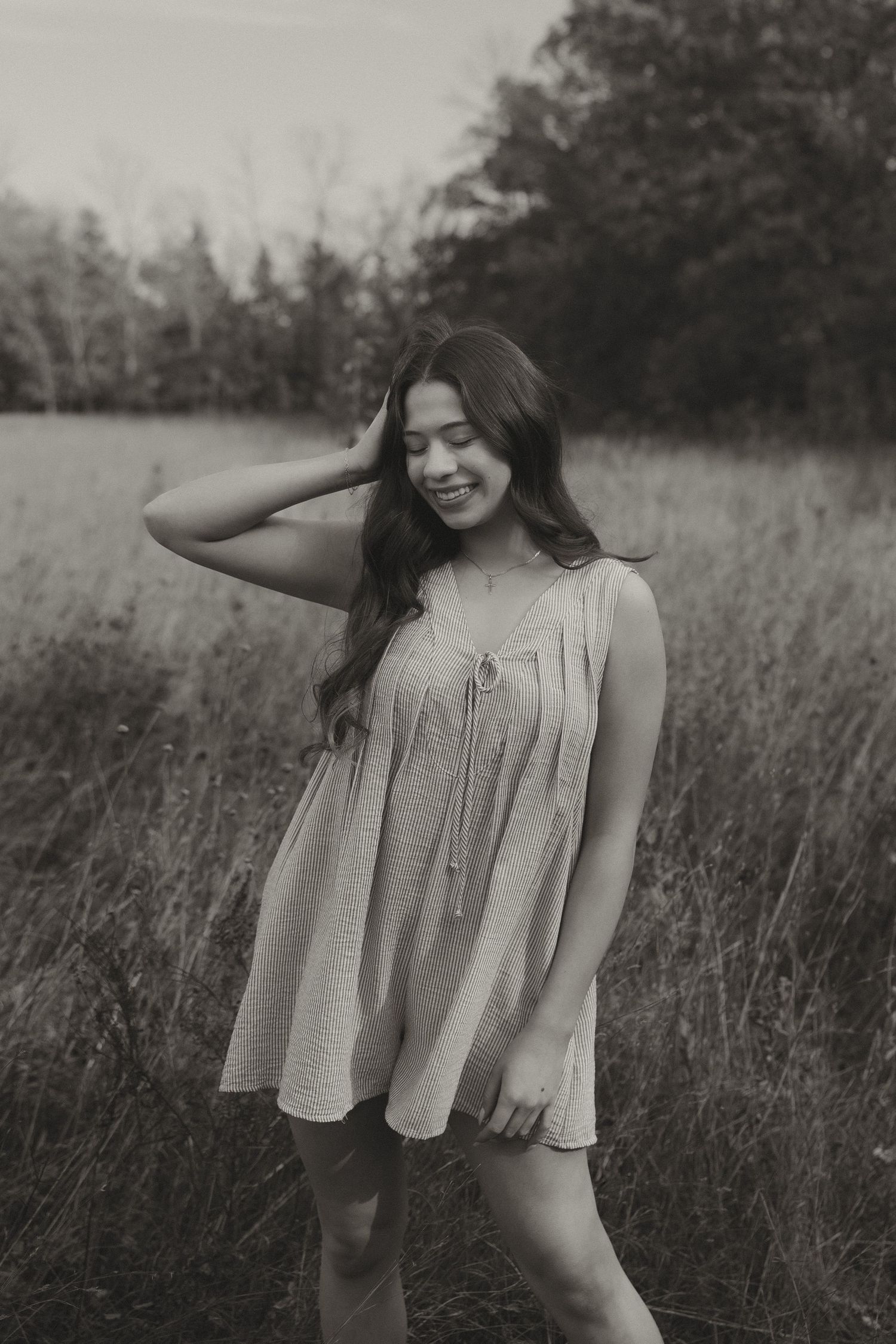Young woman in flowy dress standing in field, black and white photo.