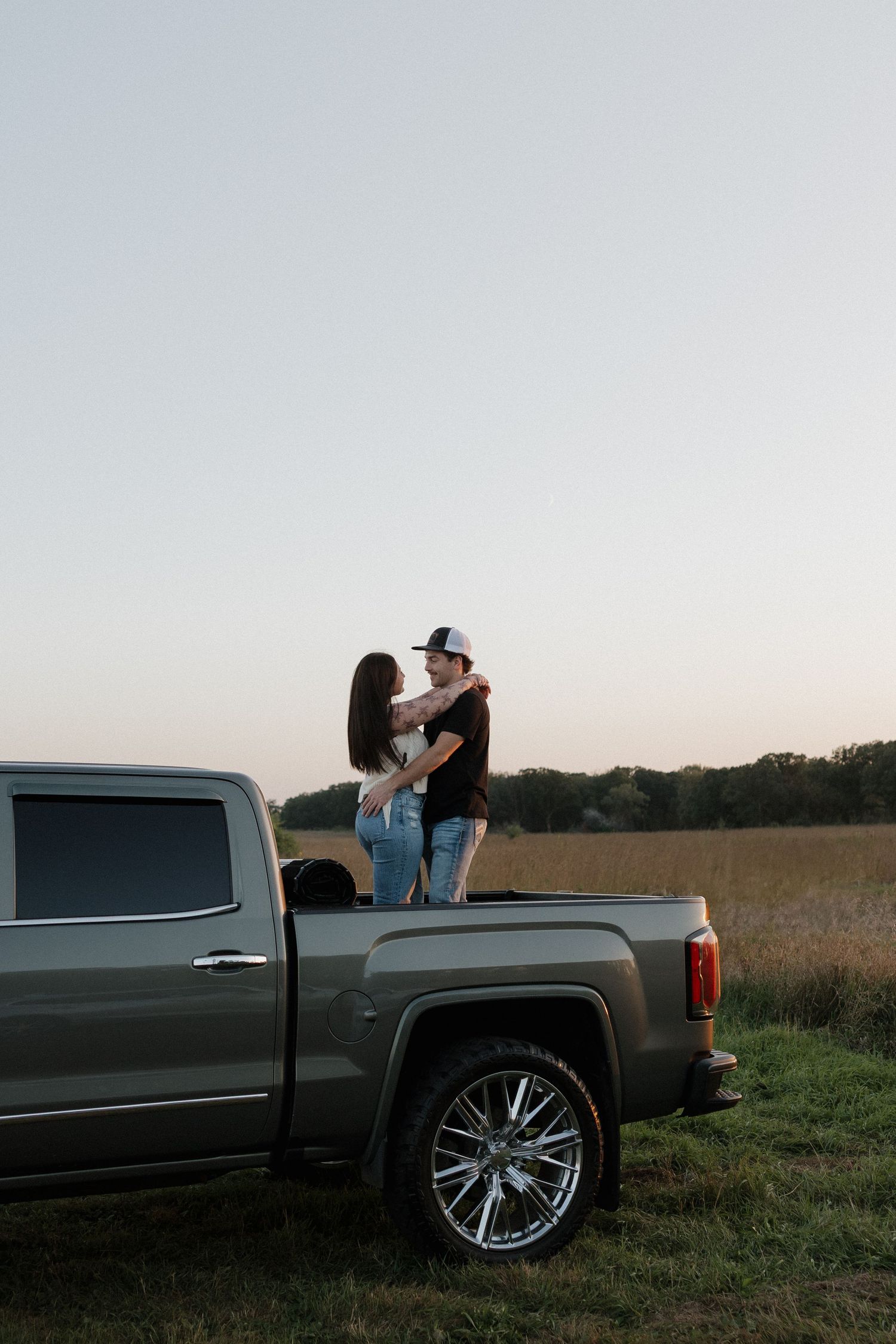 Couple embracing romantically in a truck bed overlooking a golden field at dusk.