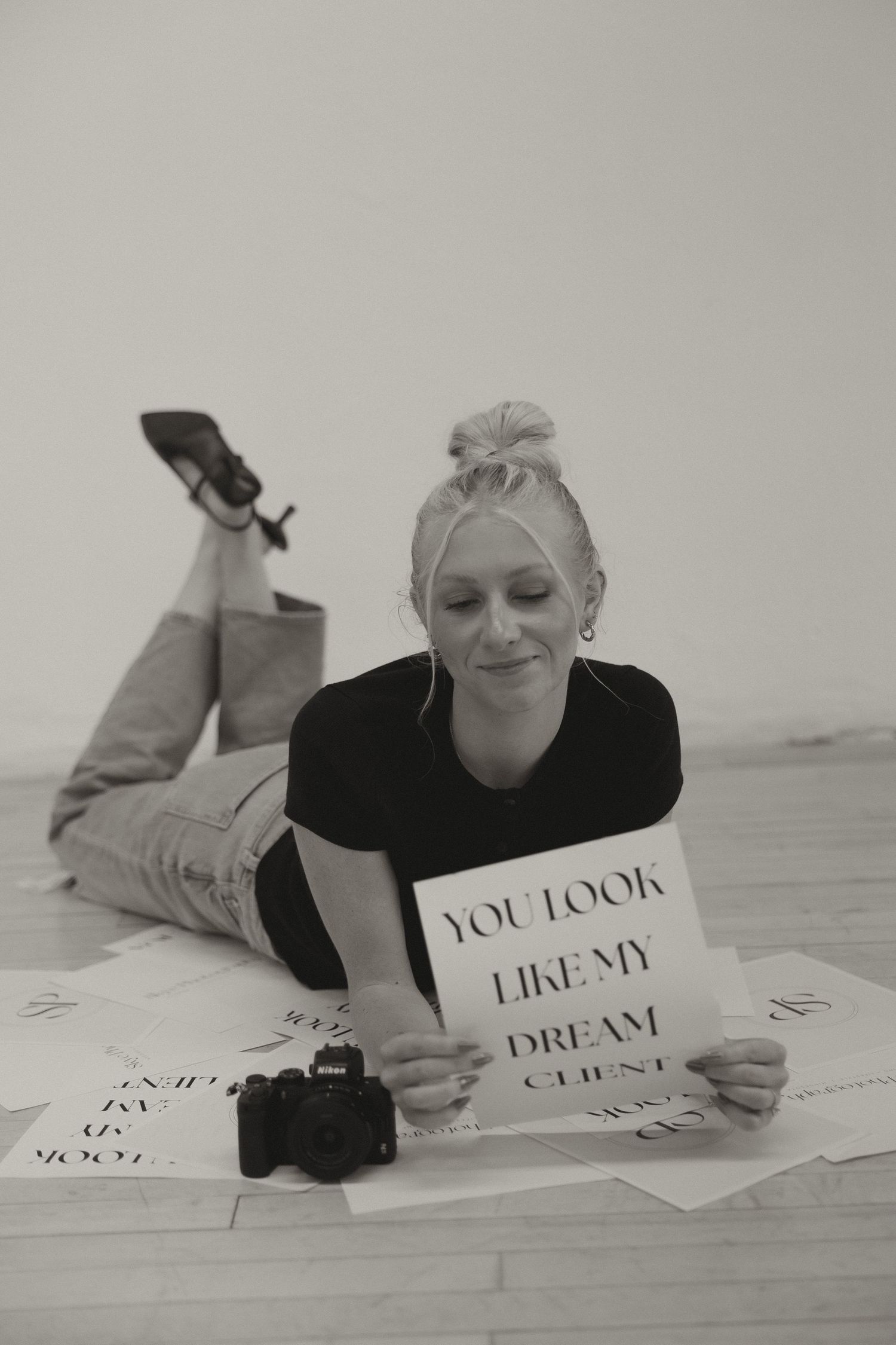 Black and white photo of woman lying on floor reading 'You Look Like My Dream Client' sign.