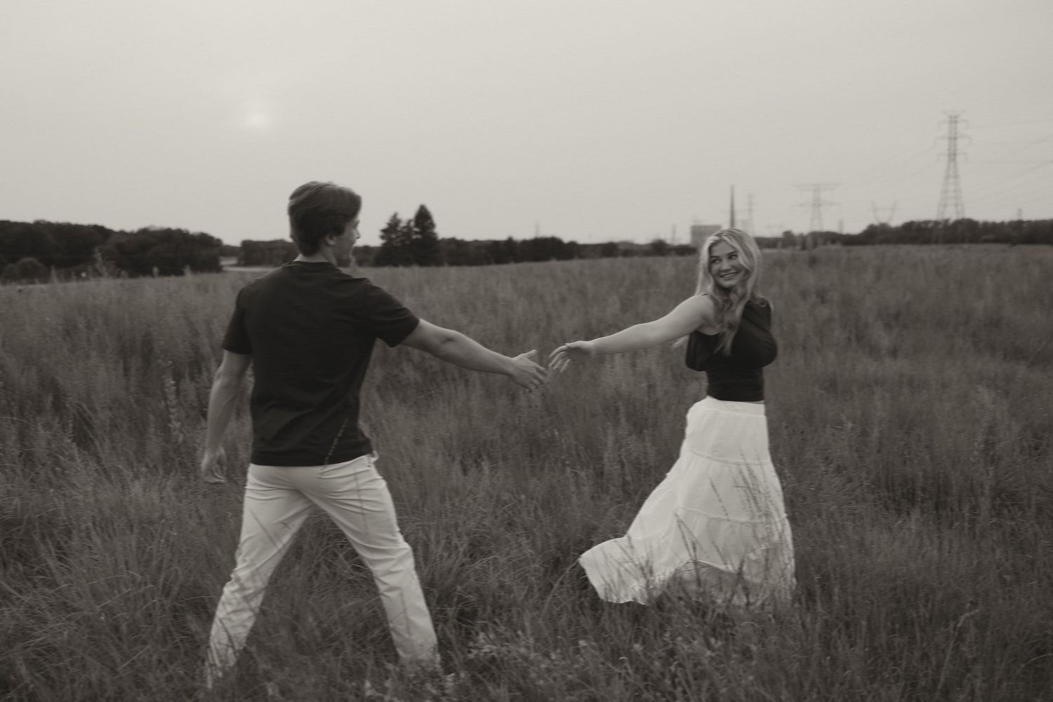 Black and white photo of a couple holding hands and spinning in an open field at dusk.