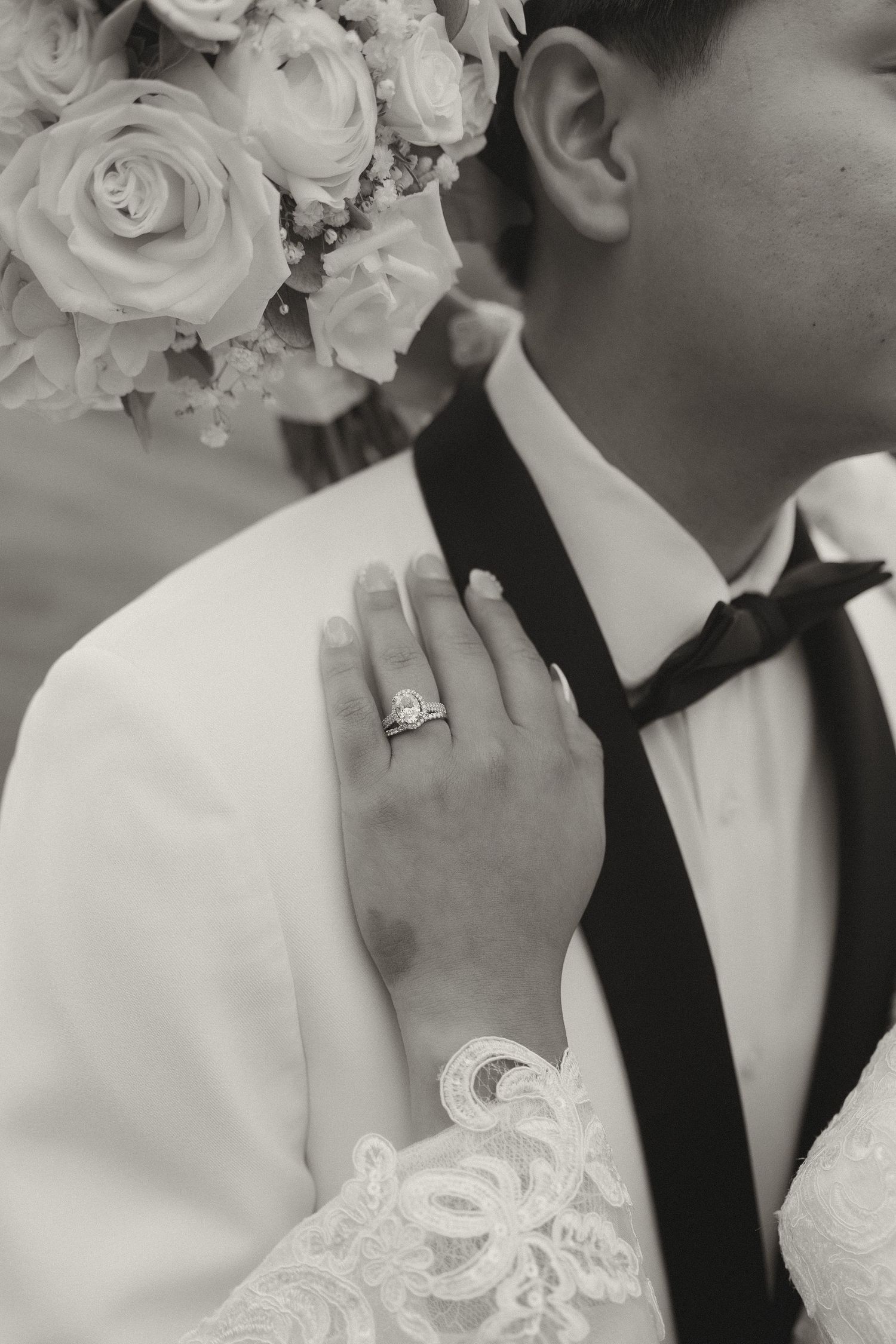 Close-up black and white photo showing wedding rings and formal attire details.