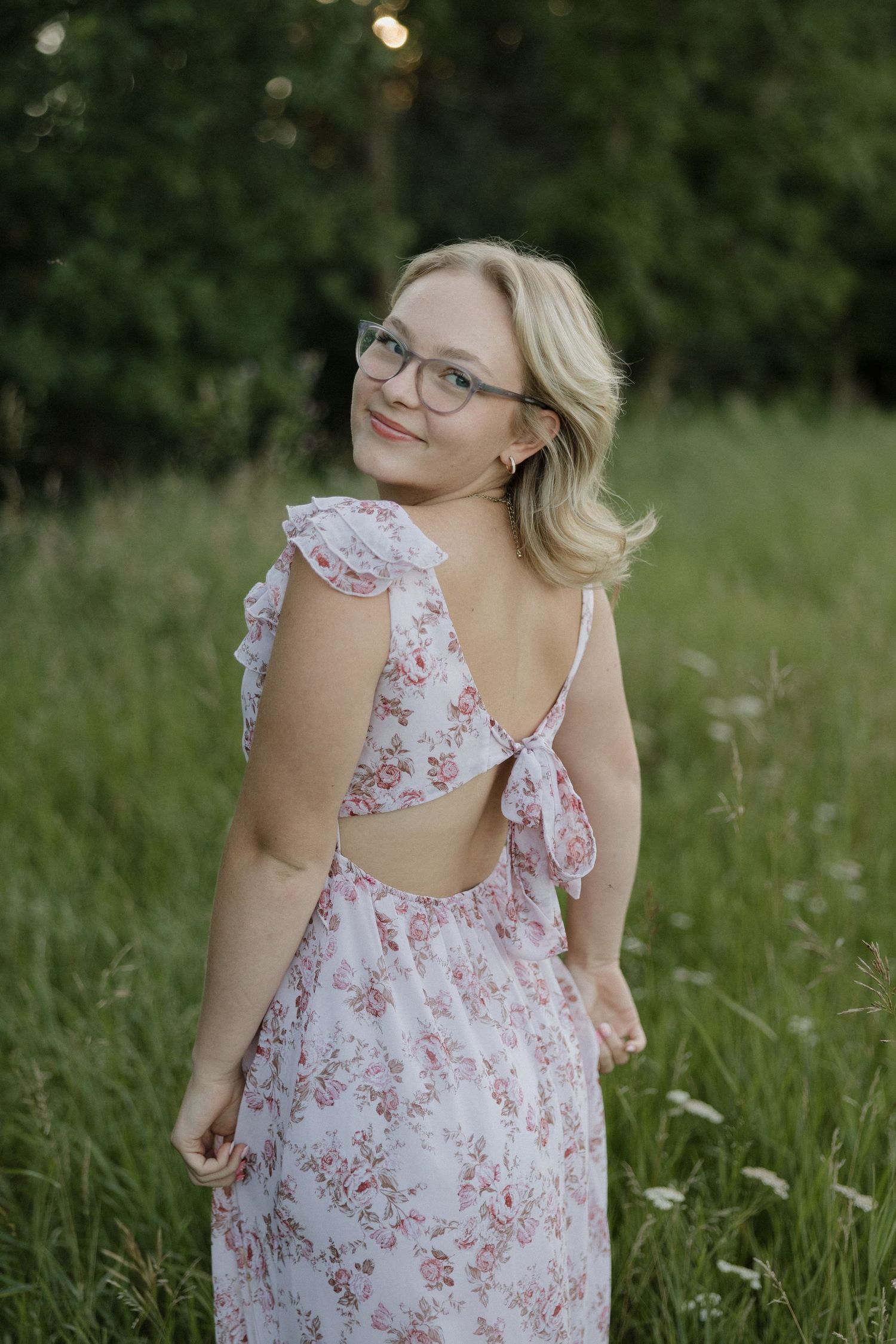 Blonde woman in floral backless dress smiling over shoulder in green field.
