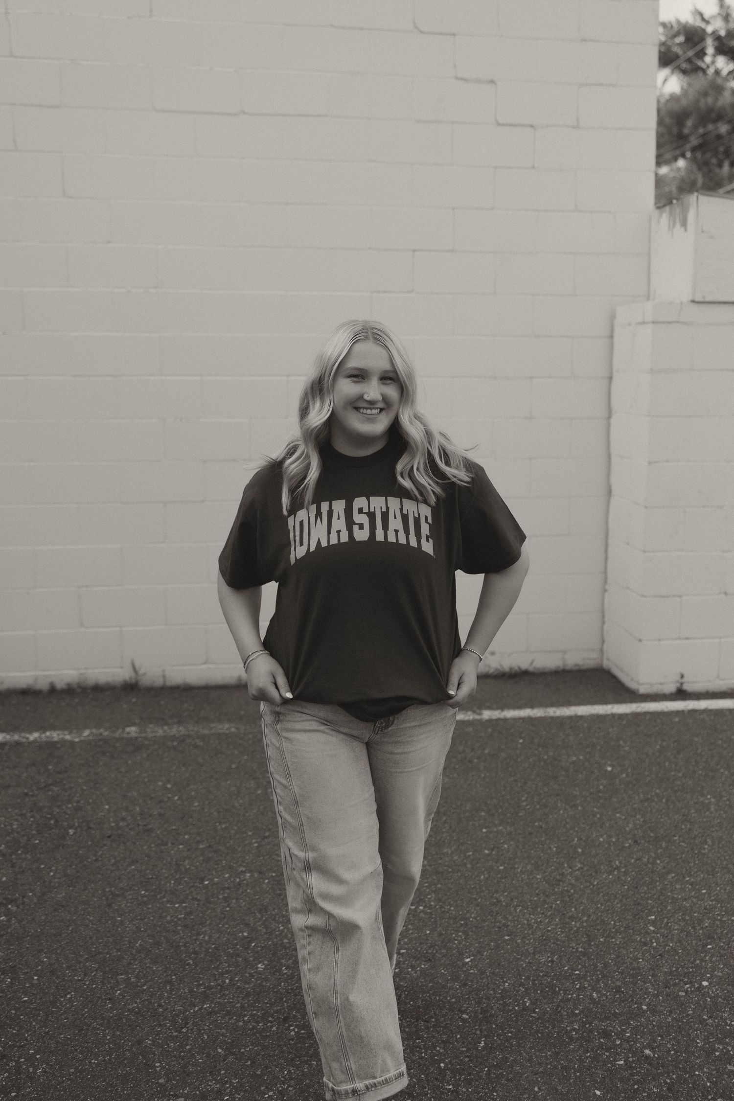 Black and white photo of blonde woman in Iowa State shirt against brick wall.