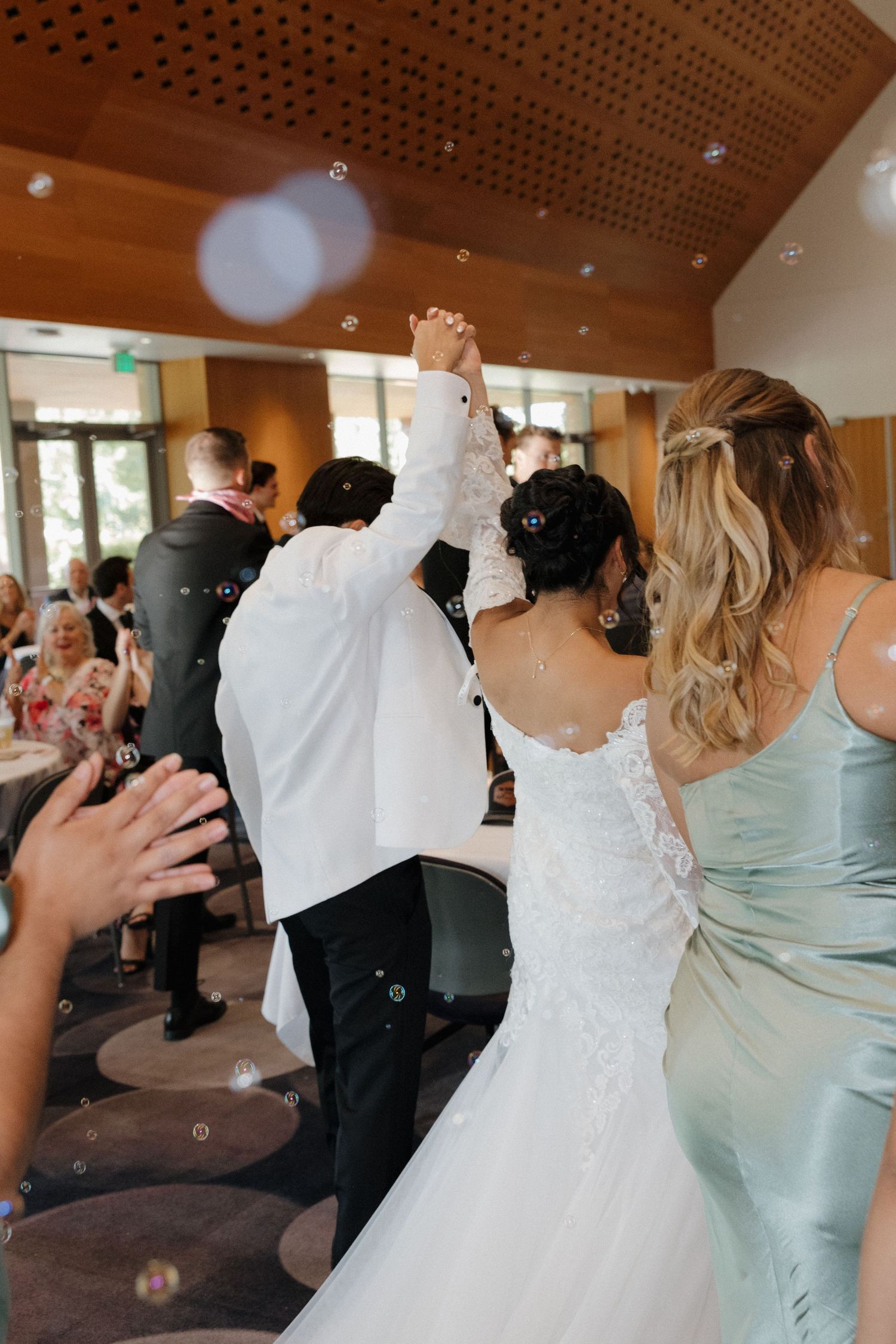Wedding celebration scene showing guests raising hands in celebration at an indoor venue.