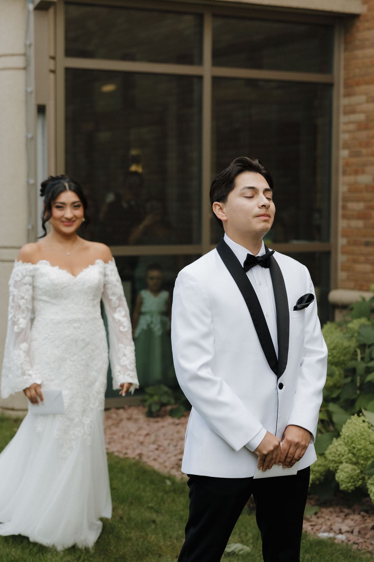 Wedding couple in white dress and black tuxedo sharing a tender moment against brick wall.