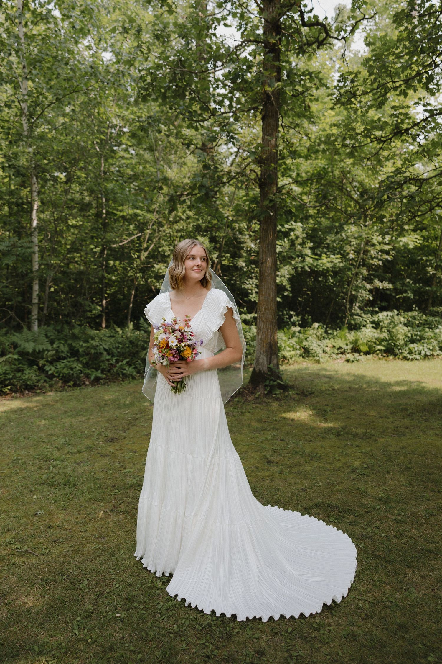 A flowing white wedding dress with lace details photographed outdoors in a natural setting.