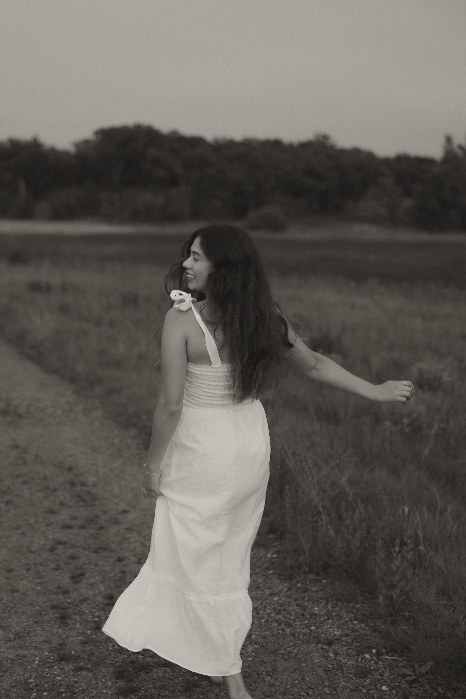Young woman in white dress walking along rural path, black and white photo.