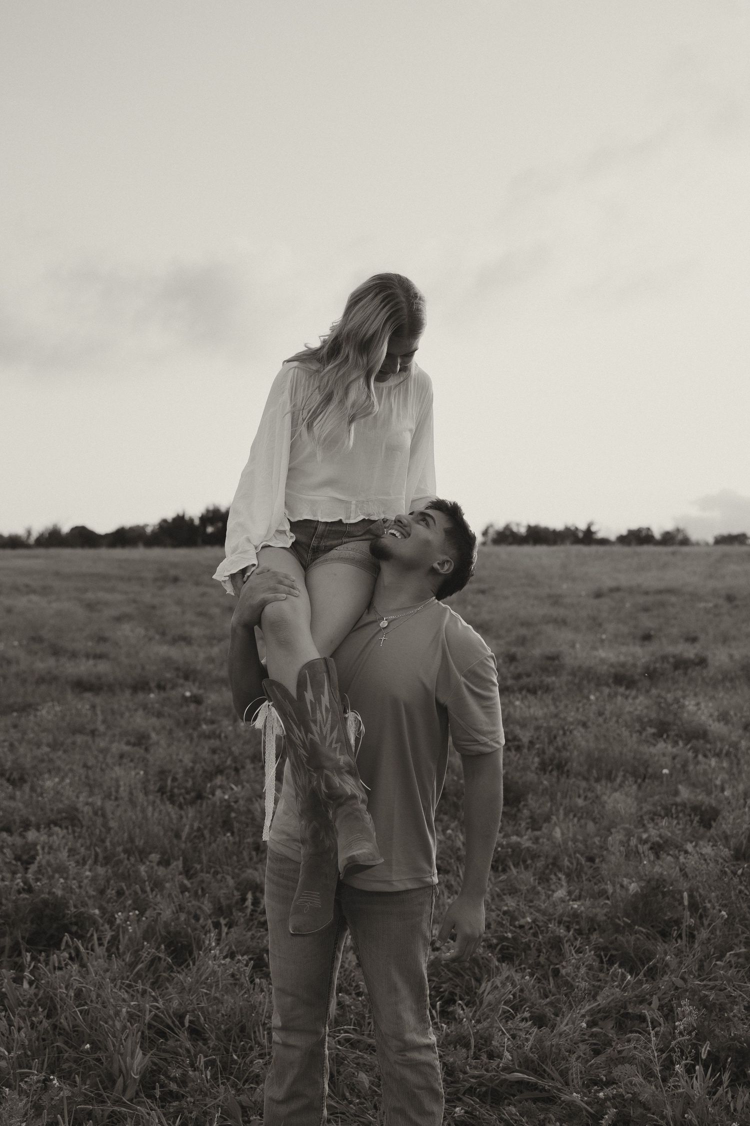 Black and white photo of man lifting woman onto his shoulders in an open countryside field.
