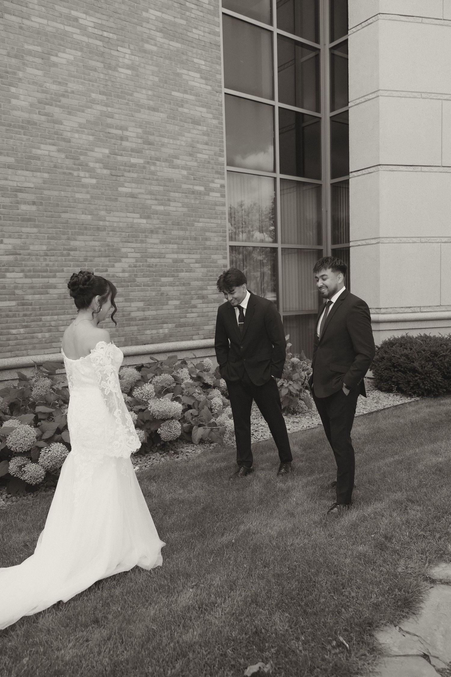 A couple takes wedding photos outside a modern brick building with landscaping.