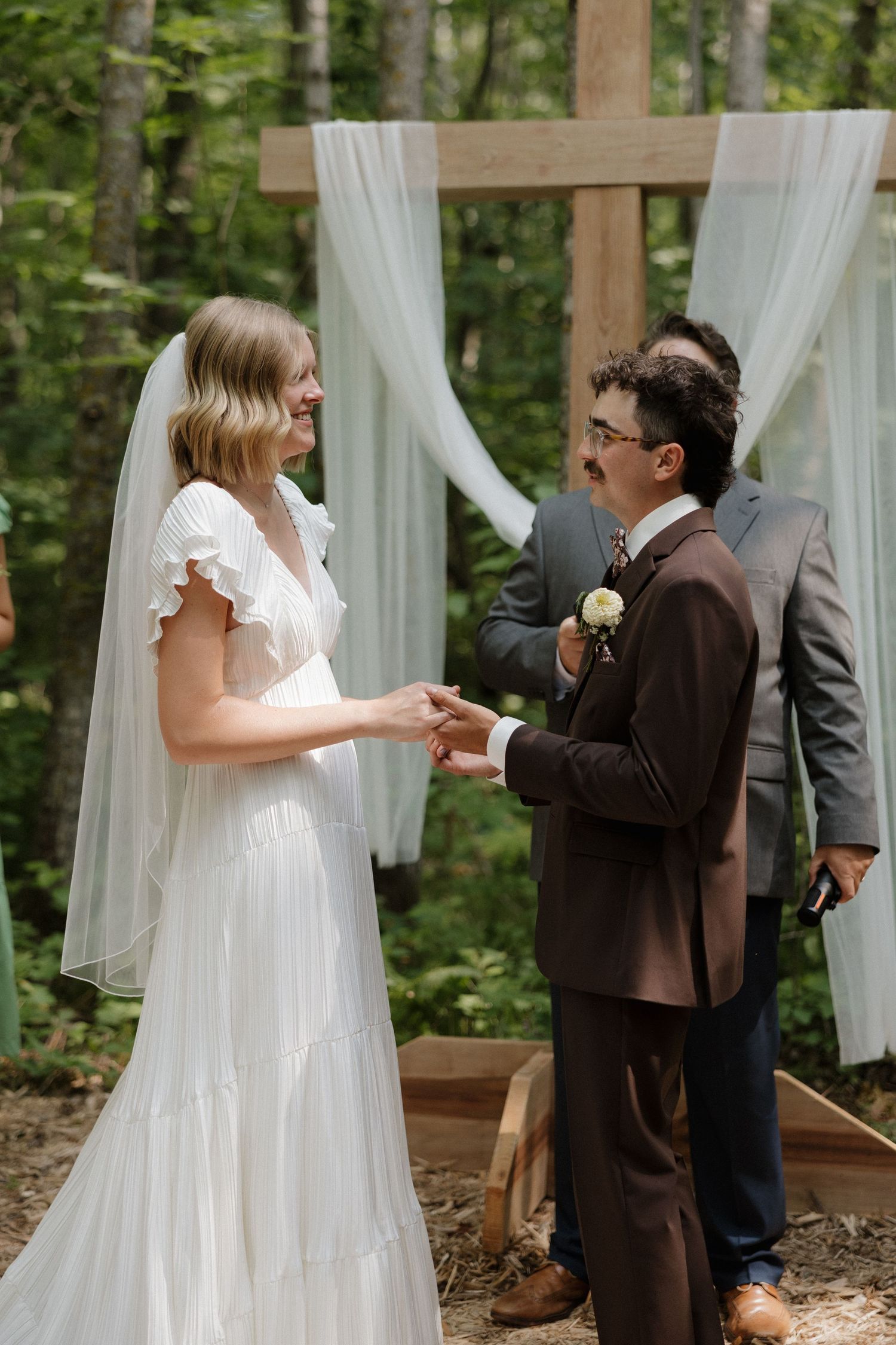 Outdoor woodland wedding ceremony with white draped altar and couple exchanging vows.
