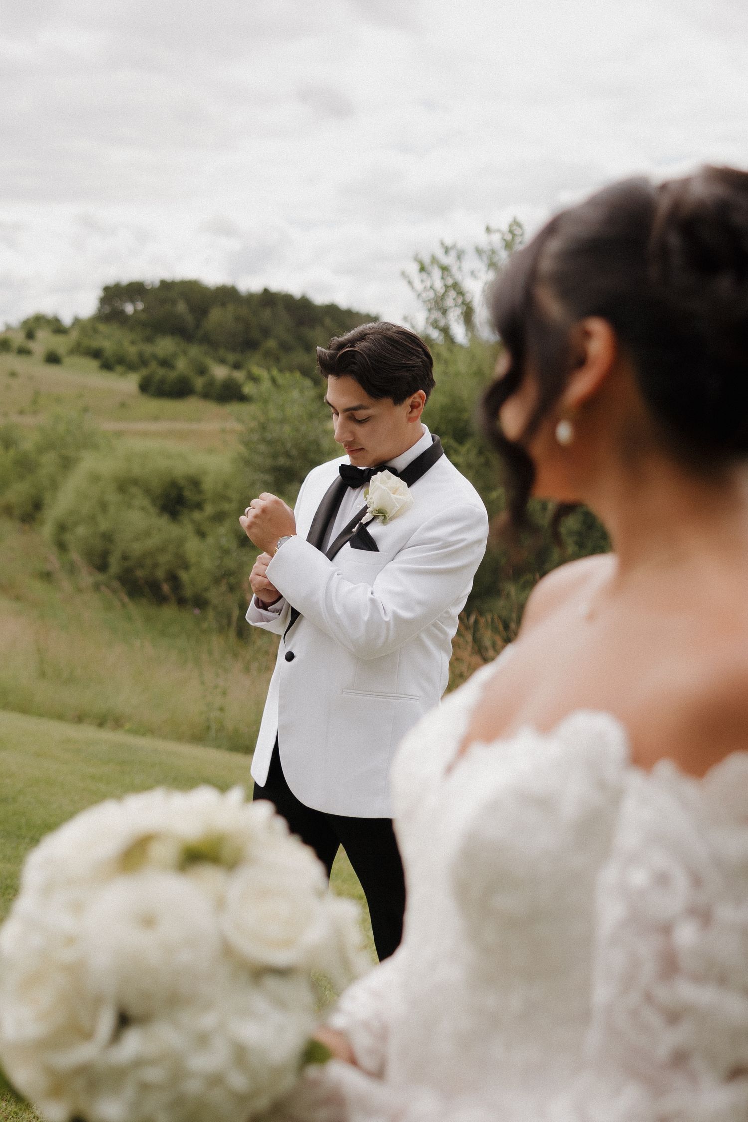 Wedding party members in formal attire posing on grassy hillside.