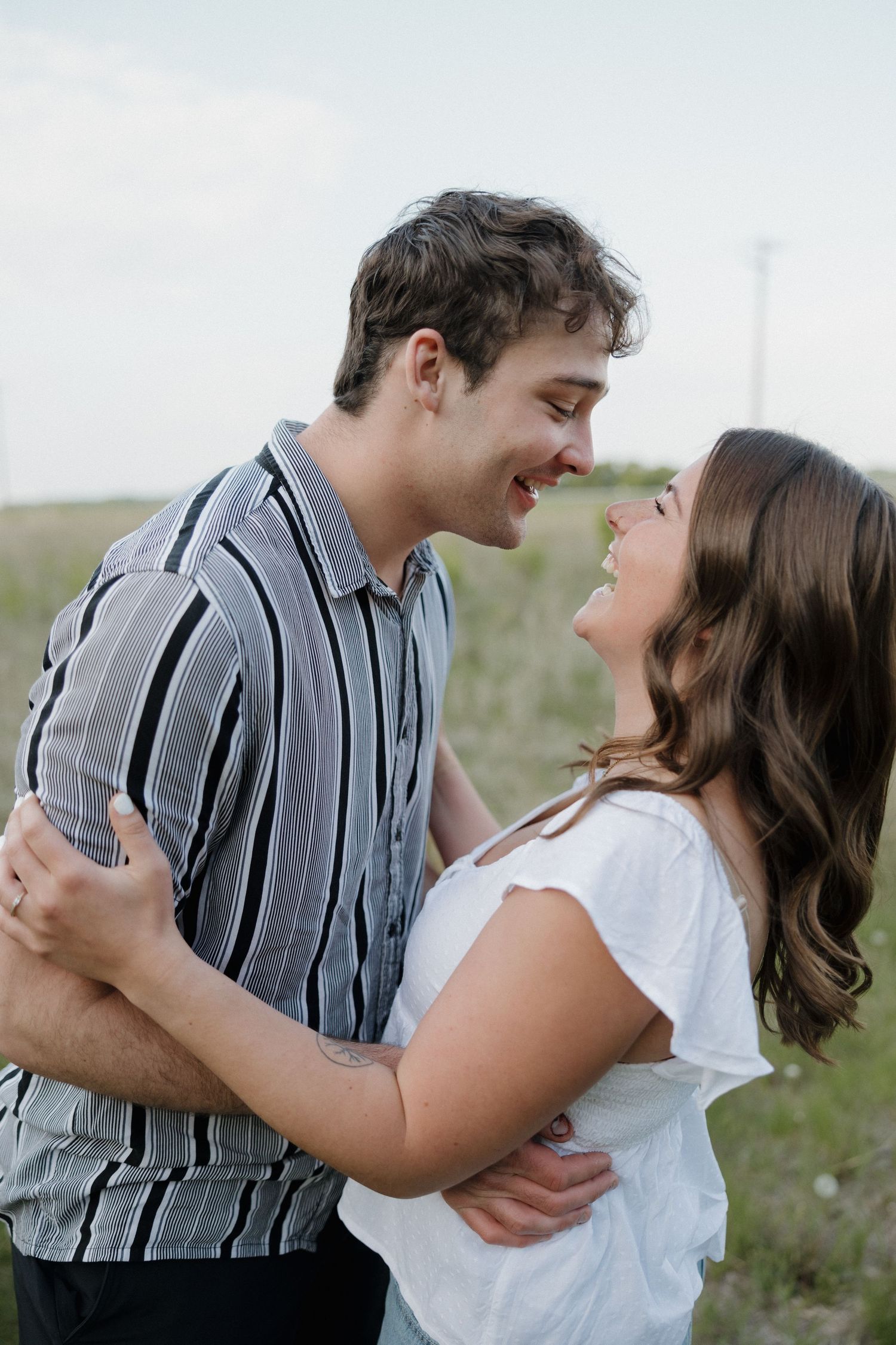 Happy couple in striped shirt and white top smiling face to face in outdoor field setting.