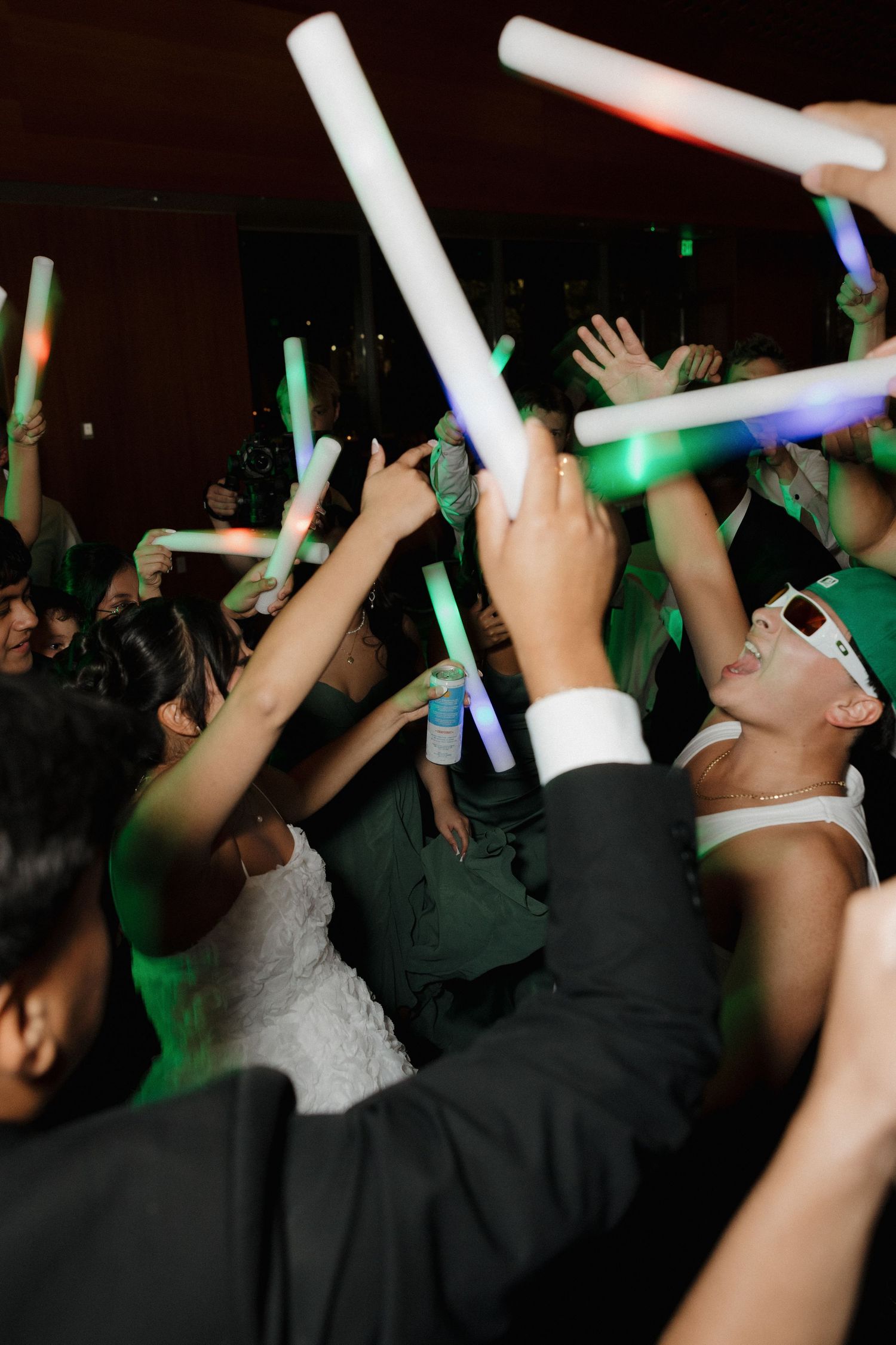 Wedding guests raise glowing foam sticks while dancing at a reception.