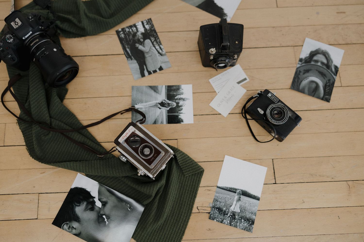 Vintage cameras and black-and-white photos arranged on a wooden floor with a green cloth.