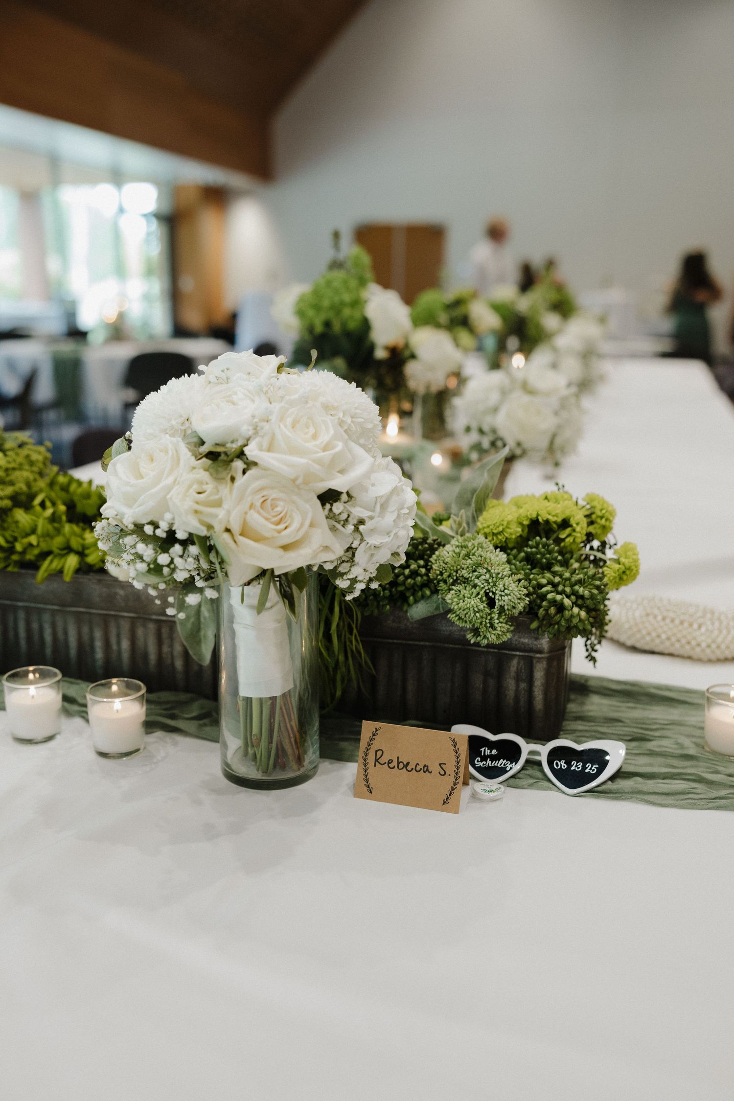 Elegant wedding table centerpiece featuring white roses and greenery with decorative sunglasses.