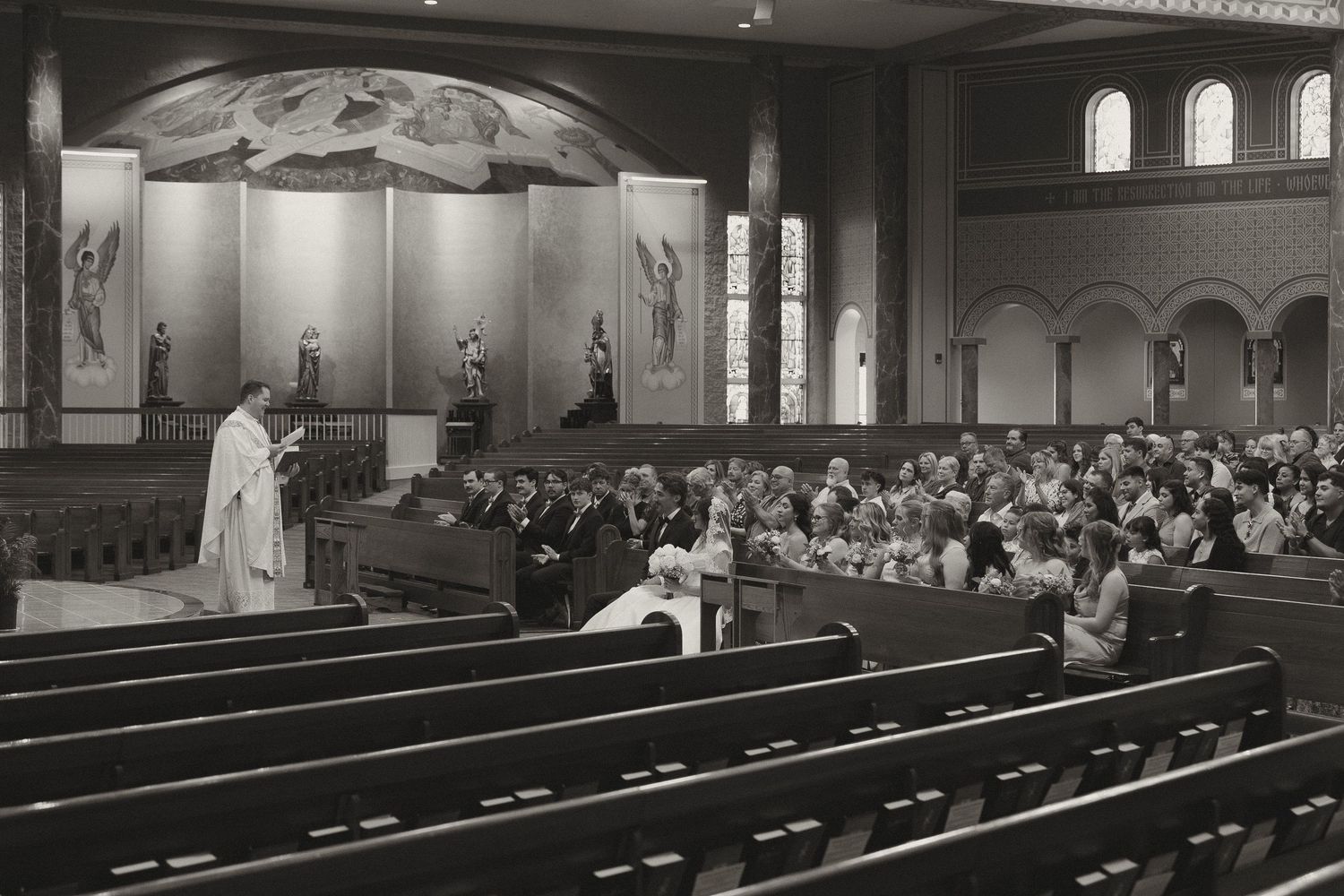 A panoramic black and white photograph shows people seated in church pews during a religious service.