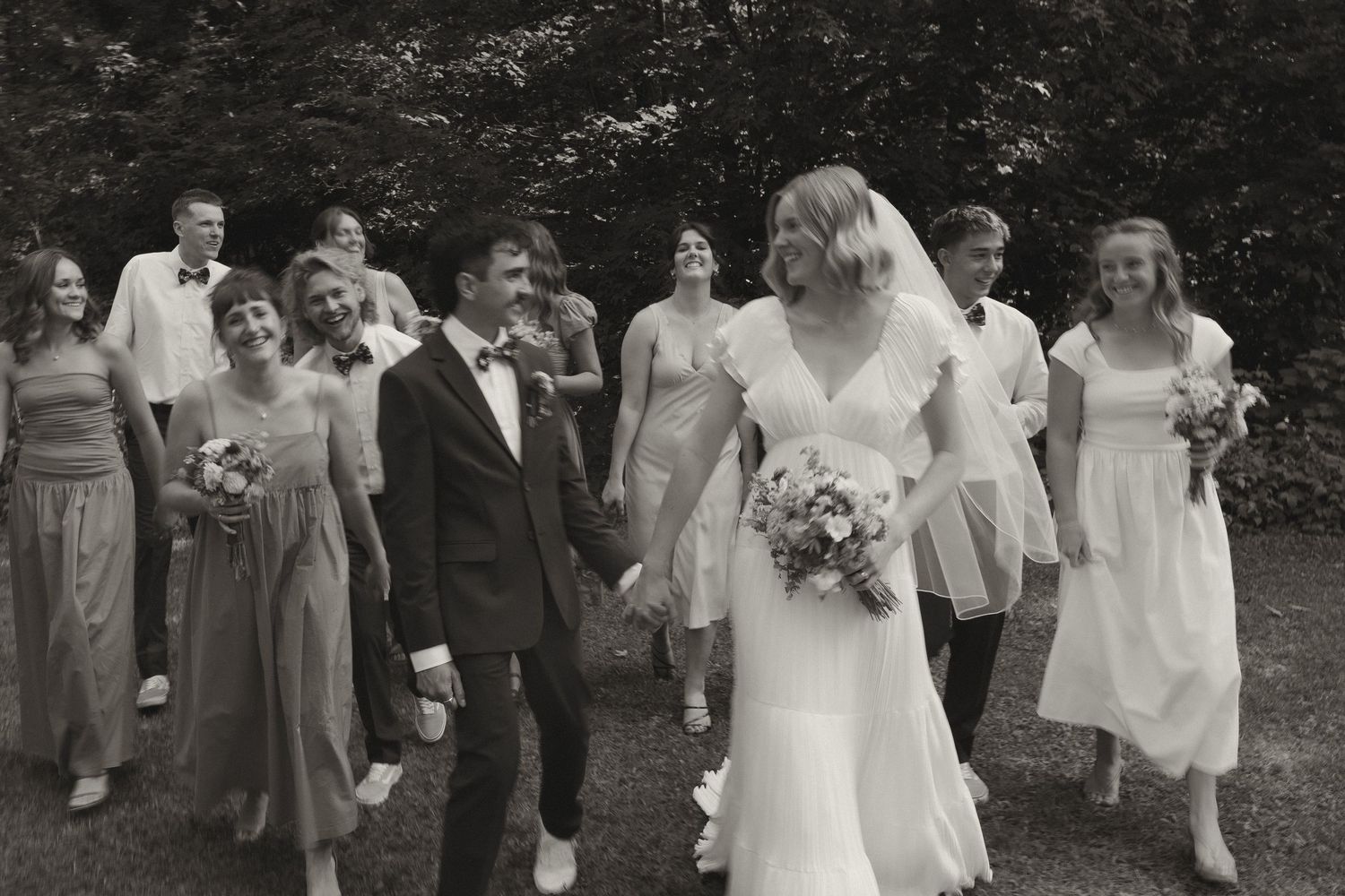 Bride and groom lead wedding party down a path in a candid black and white group photo.
