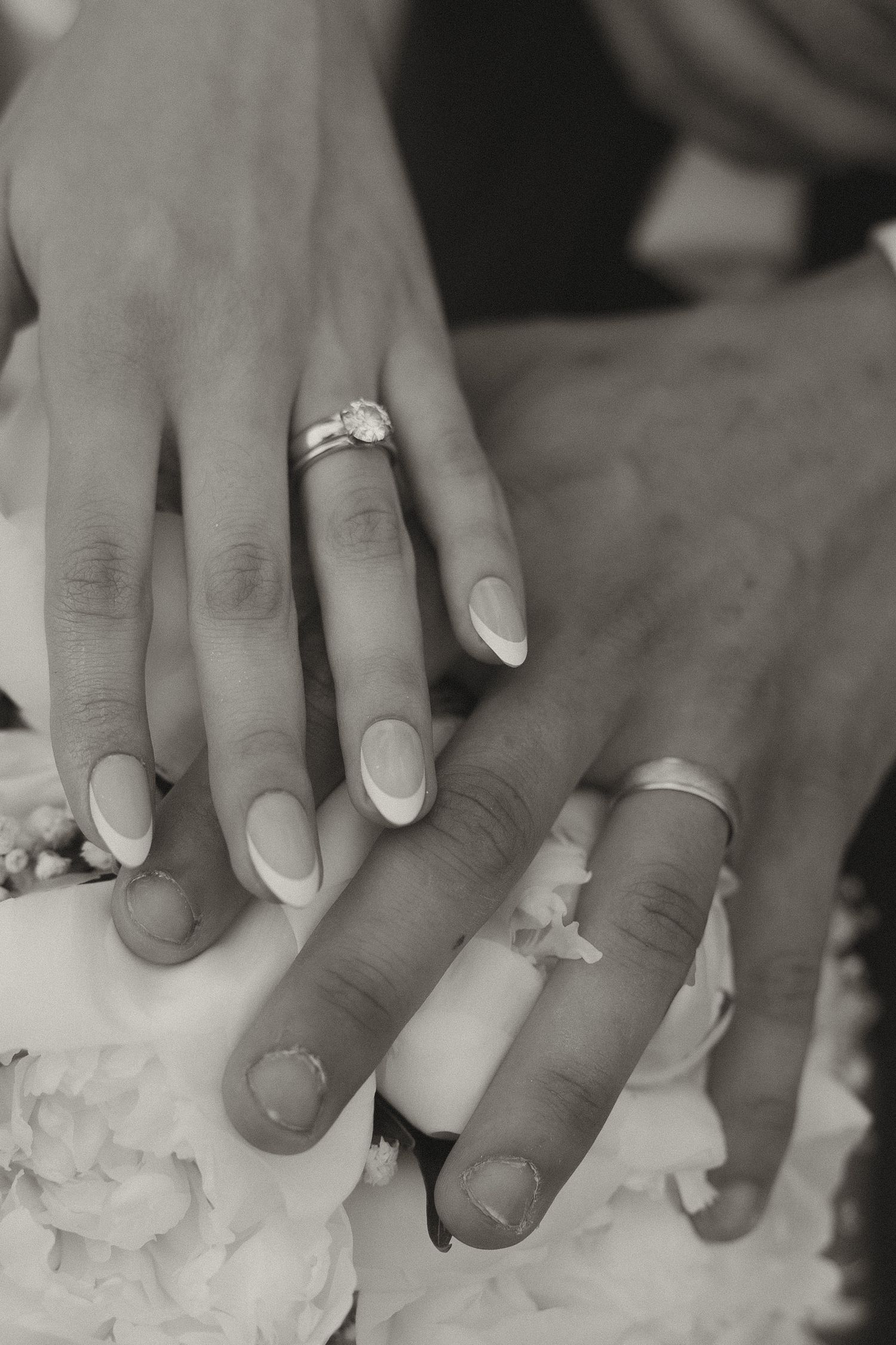 Close-up of hands wearing wedding rings touching white frosting or cake.