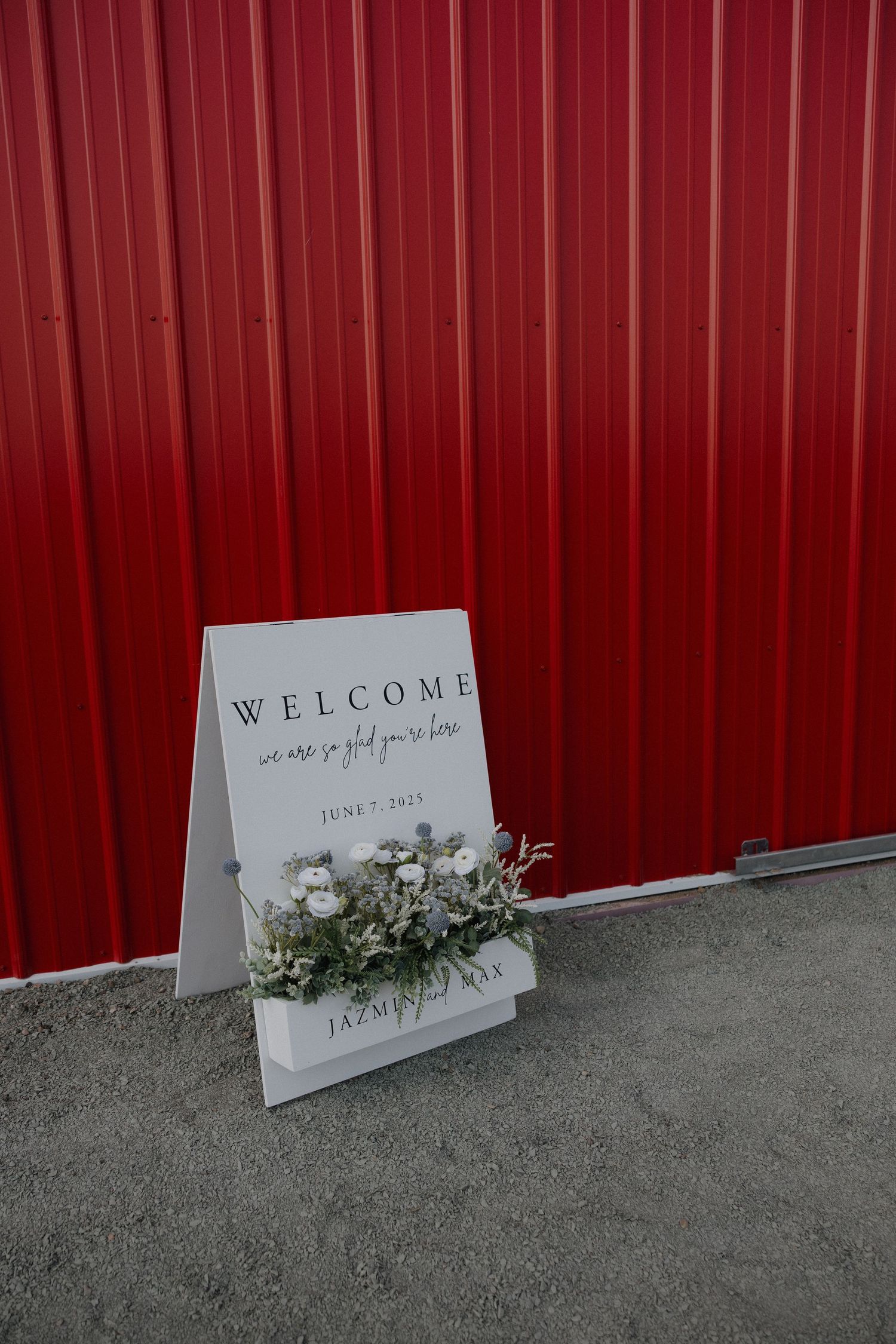Welcome sign with floral decorations sits against a red wall at a wedding venue.