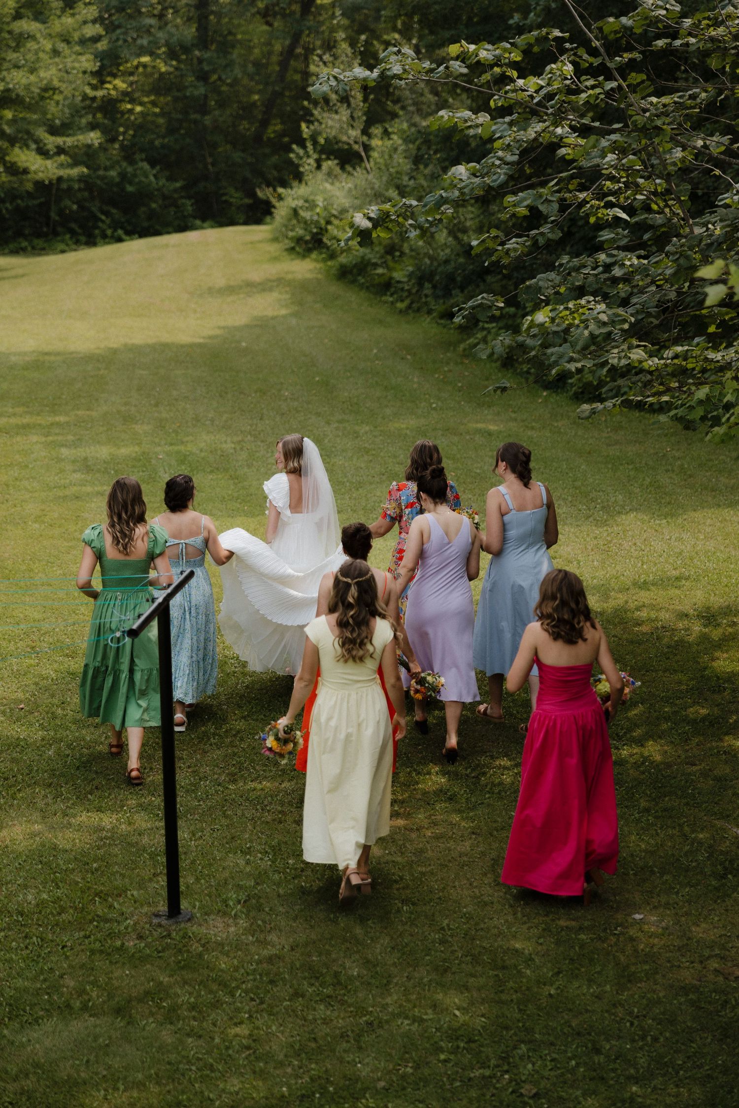 Wedding party walking through a grassy field wearing colorful dresses and formal attire.