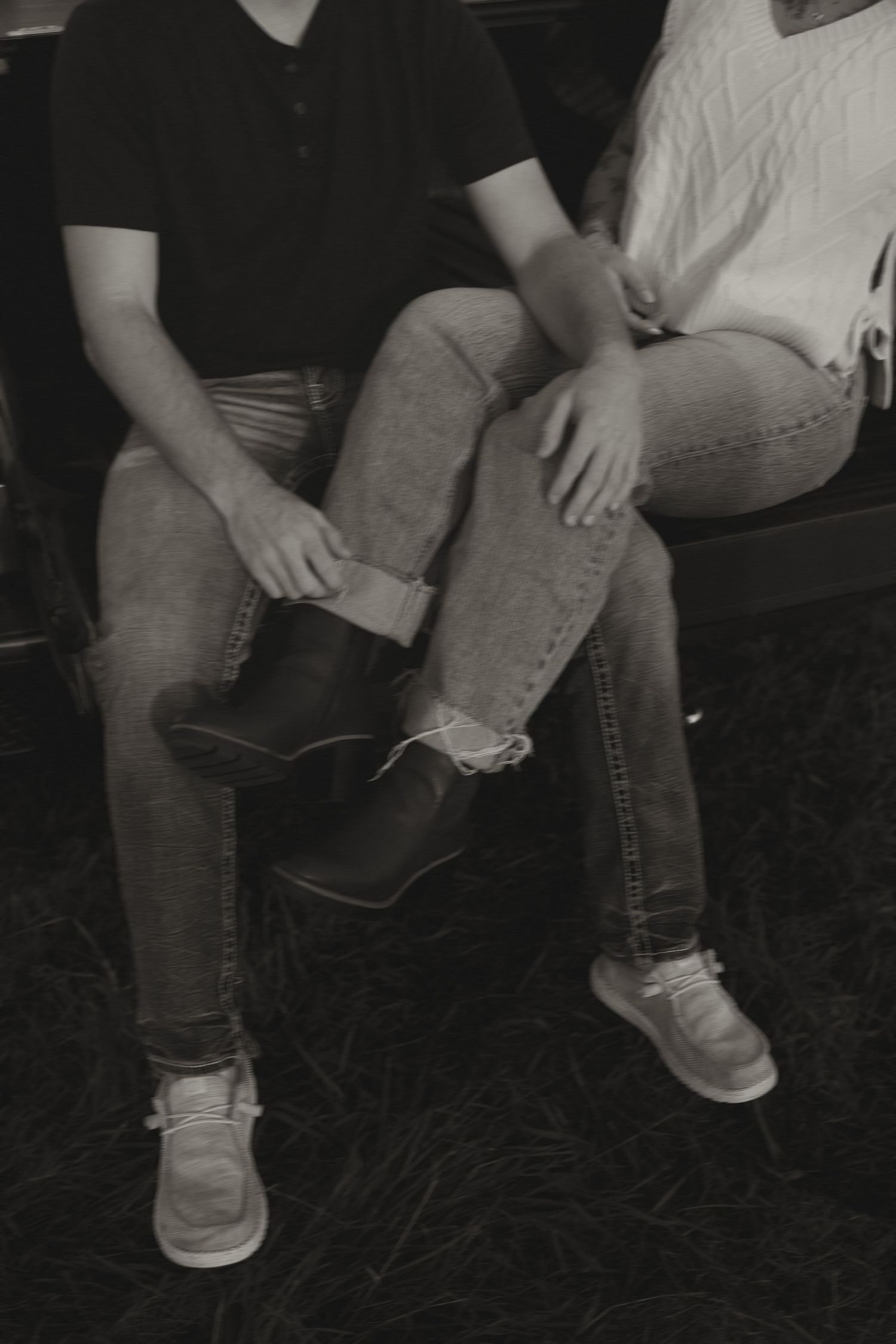 Black and white photo of couple sitting together holding hands in jeans and casual shoes.