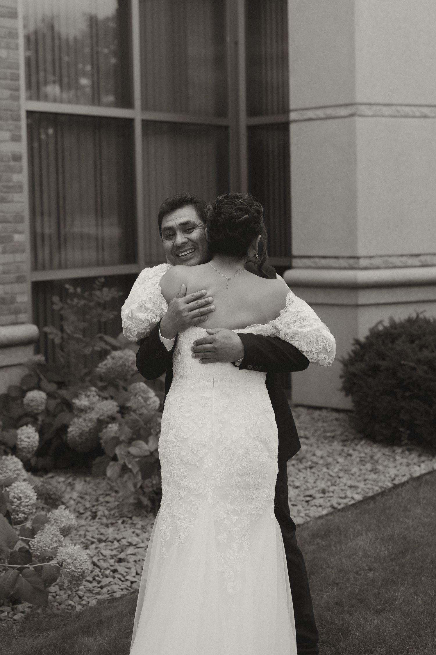 A tender moment is shared between a couple in wedding attire outside a brick building.