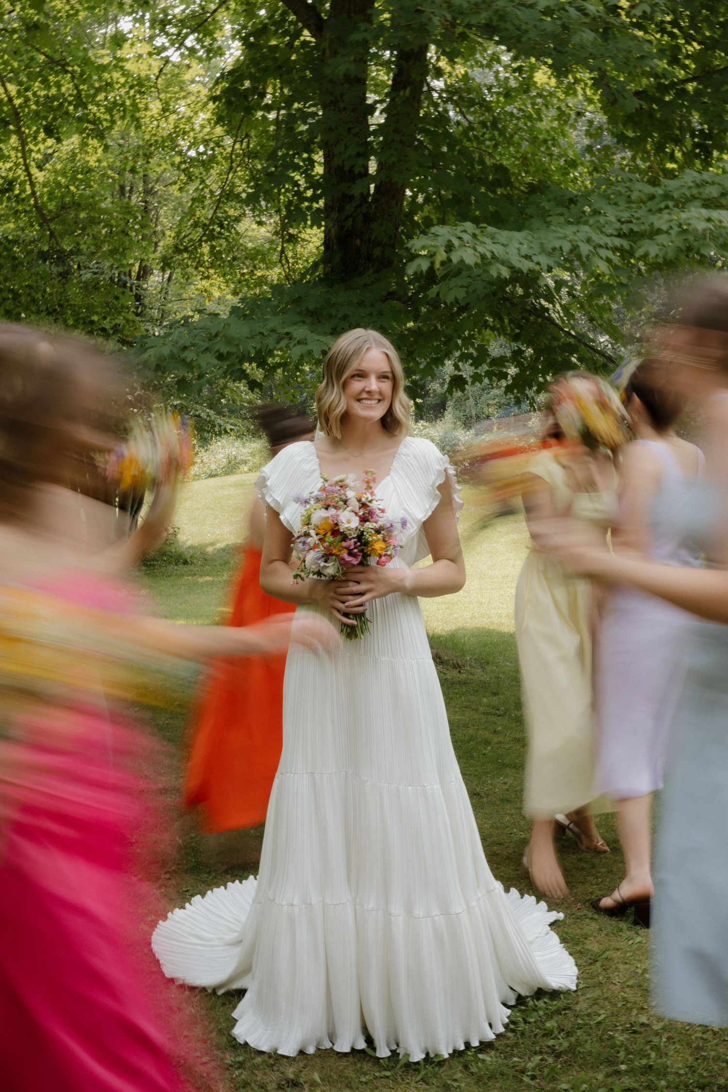 Wedding party in colorful dresses creating motion blur effect in outdoor garden setting.