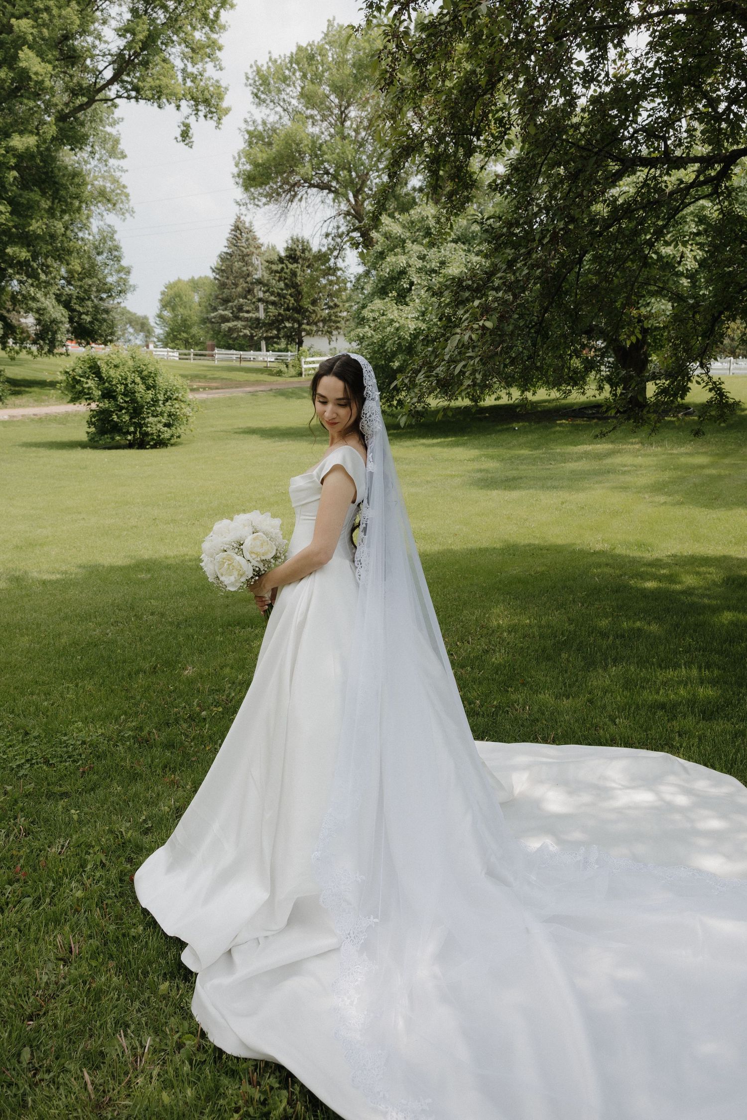 A flowing white wedding dress with a long train spreads across a lush green lawn.