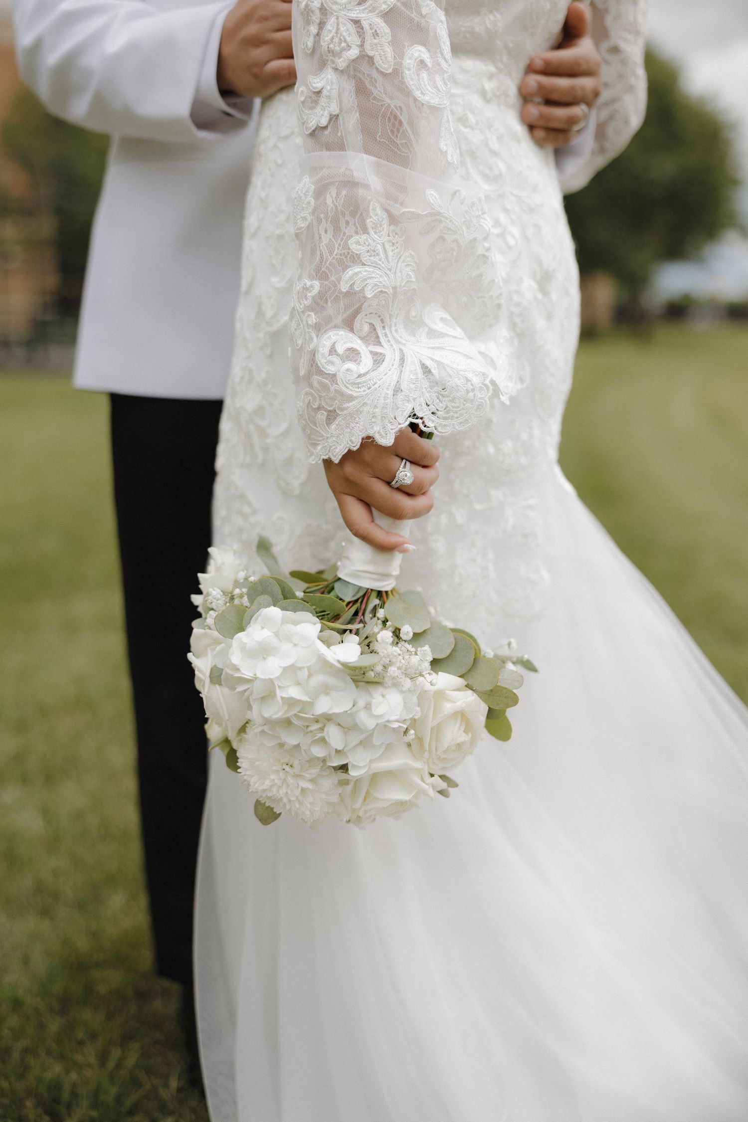 Close-up details of a white lace wedding dress with delicate floral bouquet.