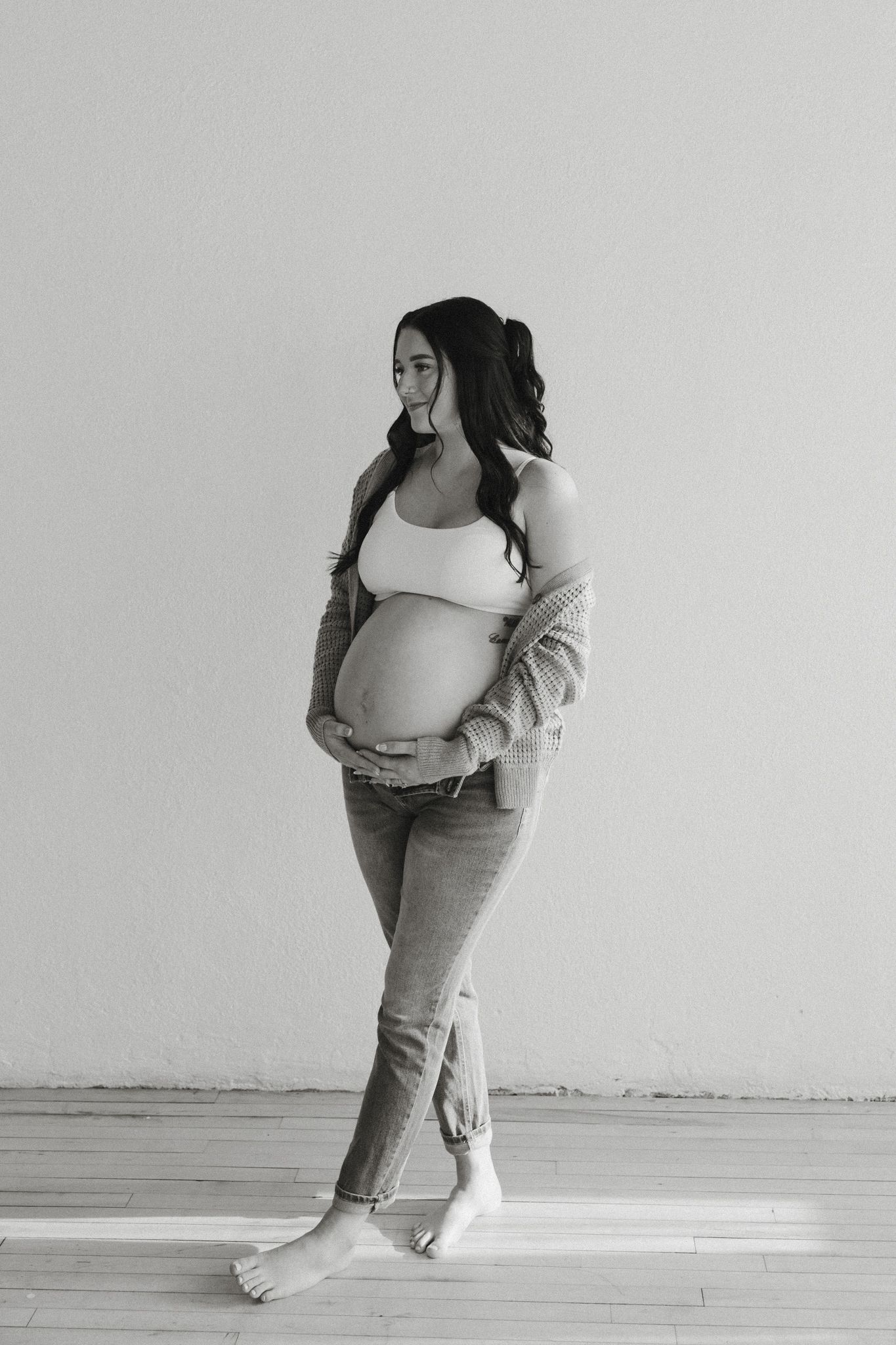 Black and white photo of pregnant woman in jeans and white crop top holding baby bump.