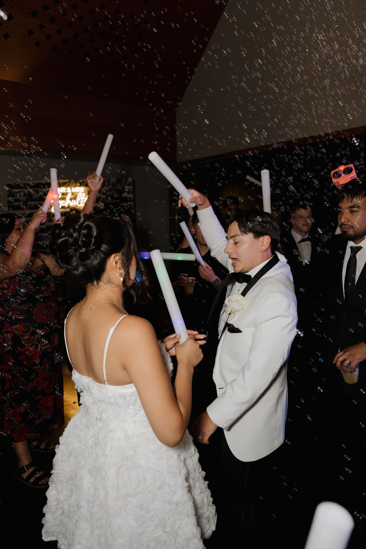 Wedding party dancing and celebrating with glow sticks at nighttime reception.
