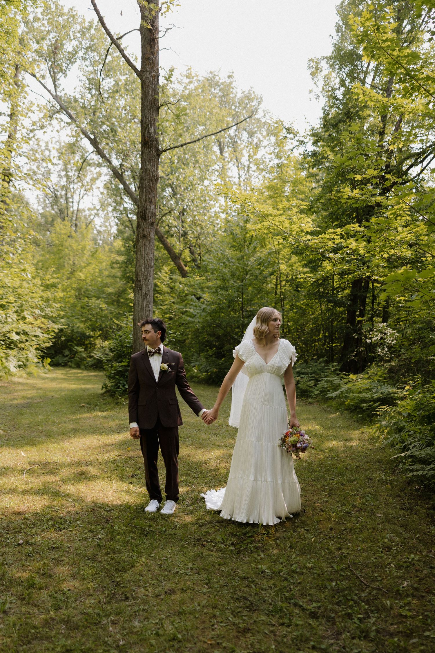 Couple walking together through a wooded outdoor path during their wedding celebration.