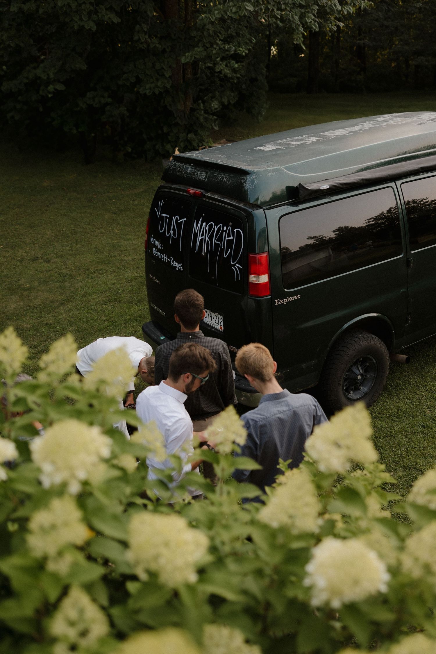 Black wedding vehicles parked on grass with white hydrangeas in foreground.