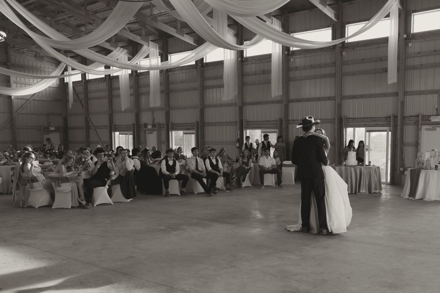Black and white panorama of a rustic barn wedding reception venue with draped fabric decorations.