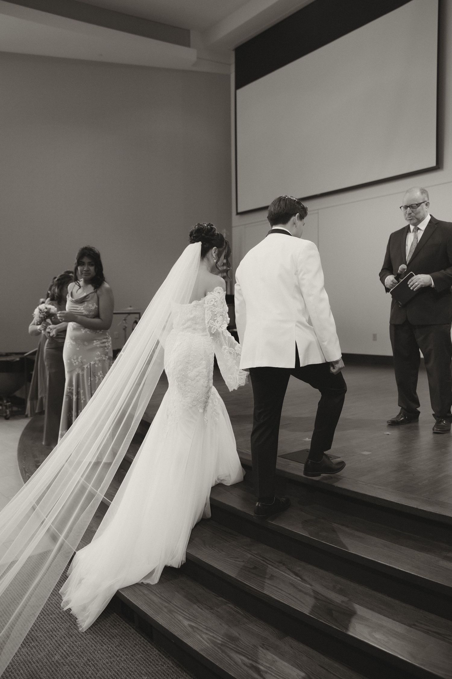 Black and white photo of bride's dress train flowing down stairs in elegant venue.