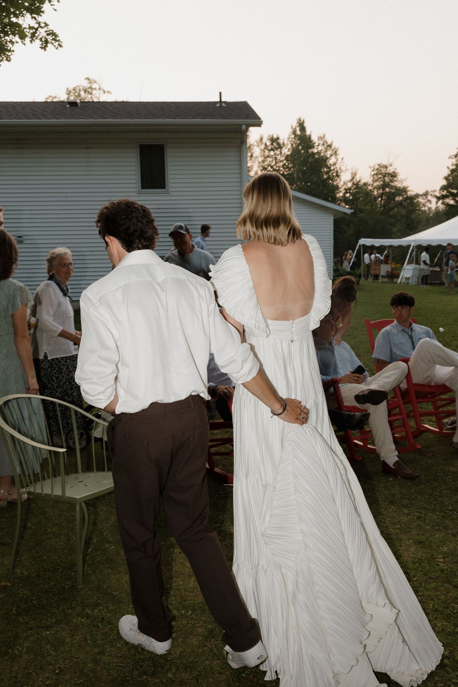 Wedding reception guests dancing on a lawn near white buildings at dusk.